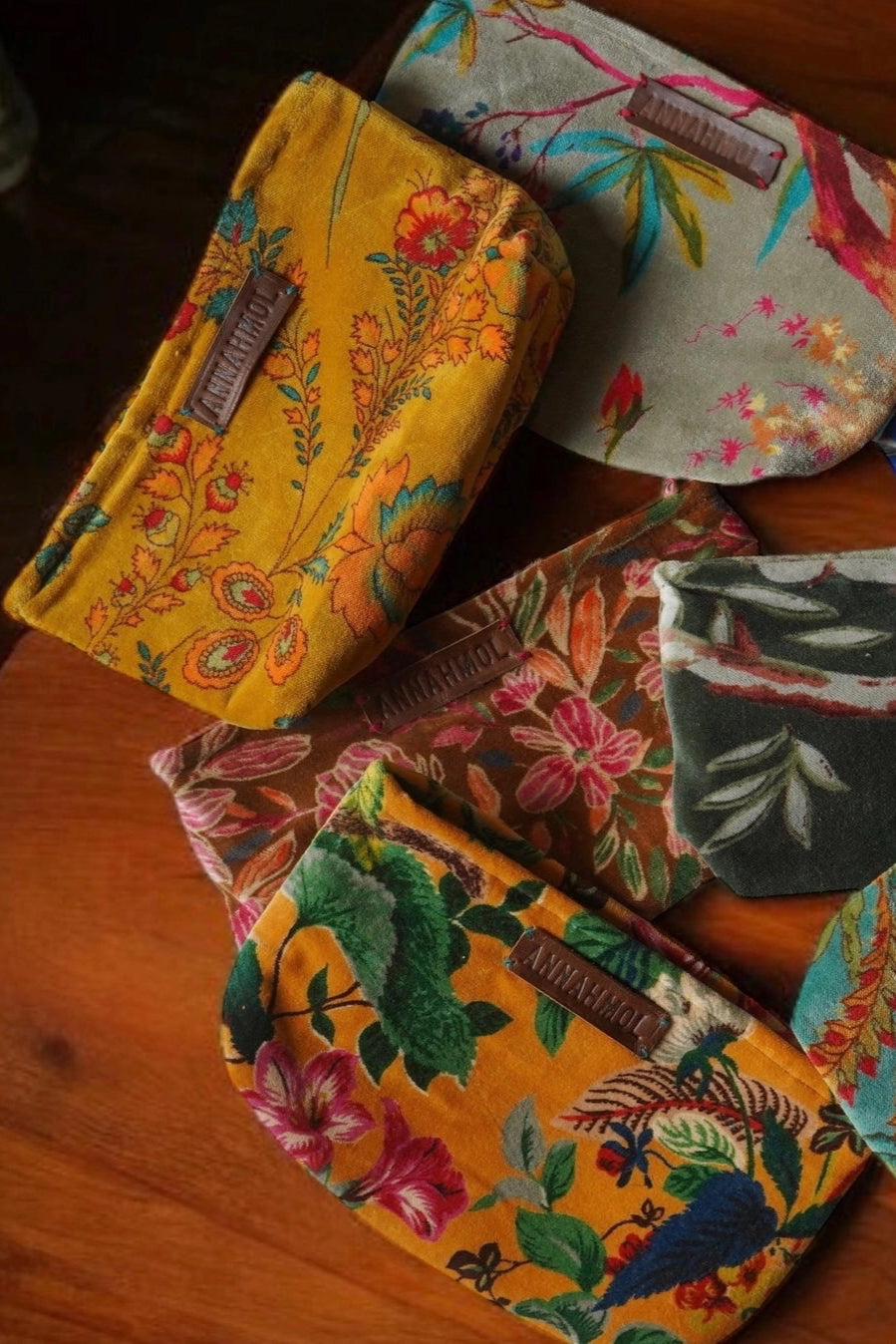 Assorted floral printed velvet pouches laying on a wood table ©Annahmol