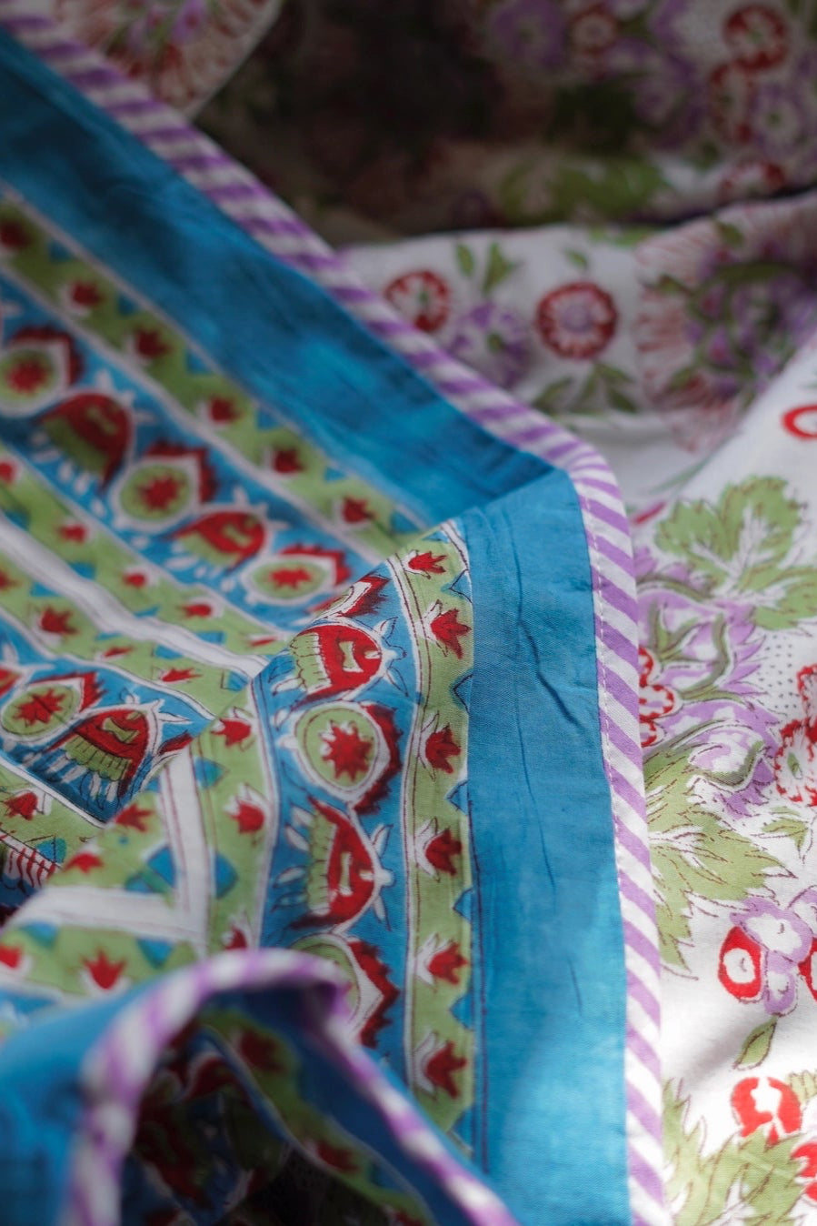 Colorful blue fabric with floral and geometric patterns showing both sides of a reversible blanket ©Annahmol