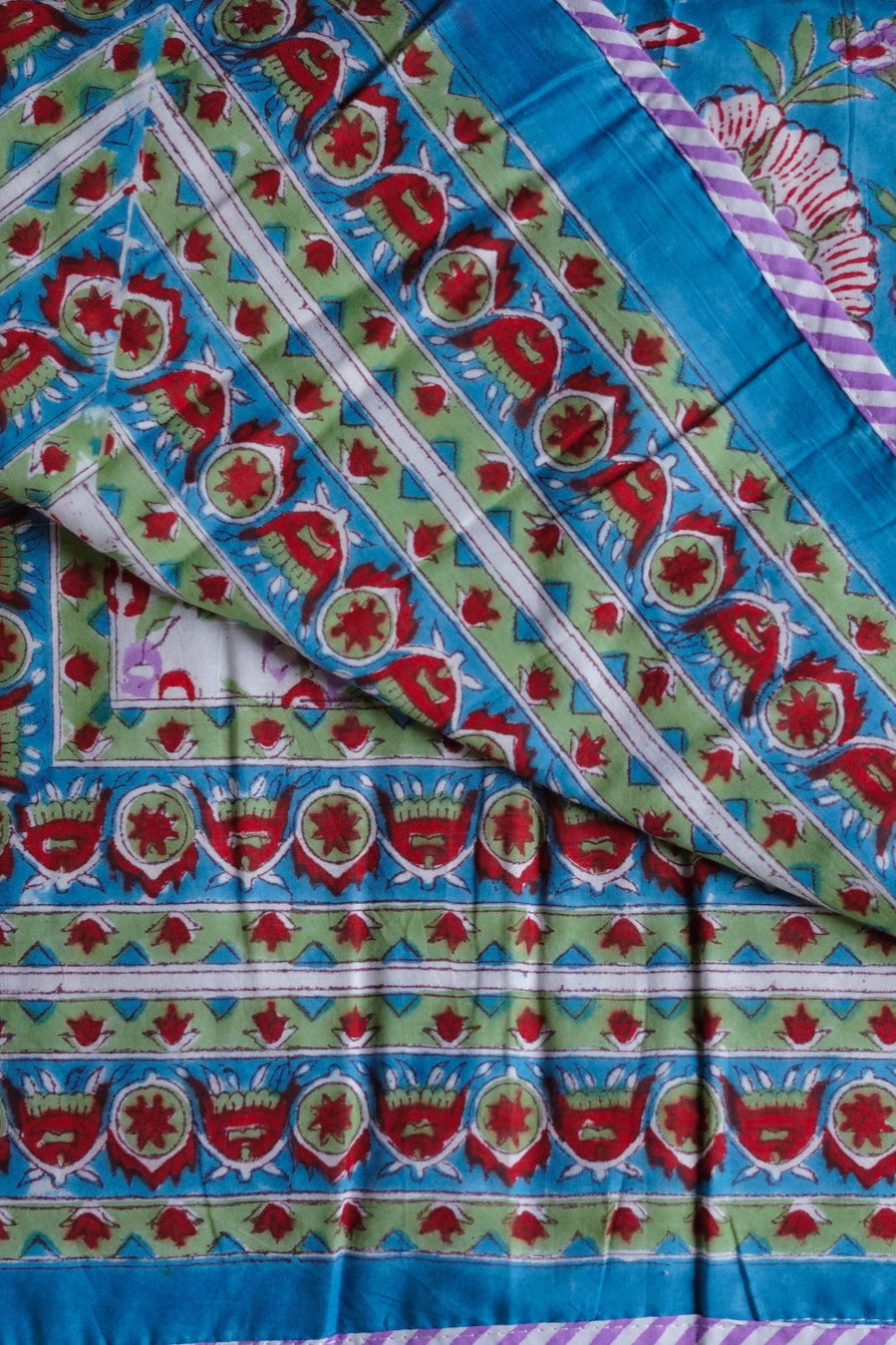 Colorful blue fabric with floral and geometric patterns of a reversible blanket ©Annahmol