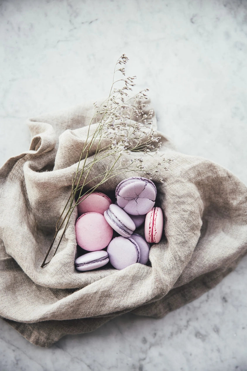 Purple and pink macaroons sitting inside a linen cloth from a page of the Flowers on a Plate book.
