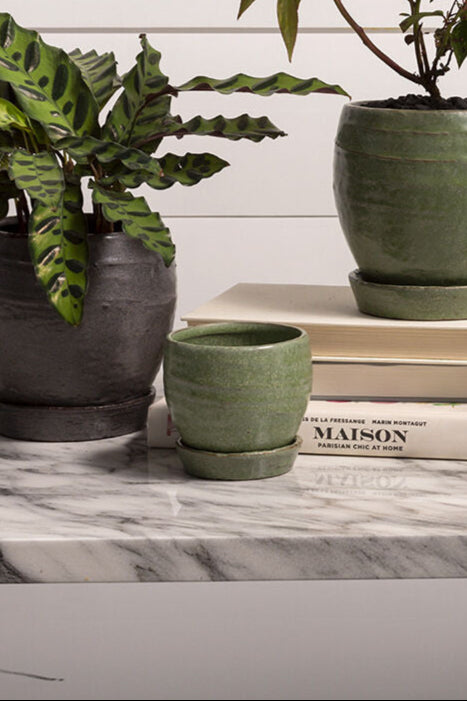 Three green ceramic pots on a marble surface with books and a plant. ©Sprout Home ©Accent Decor