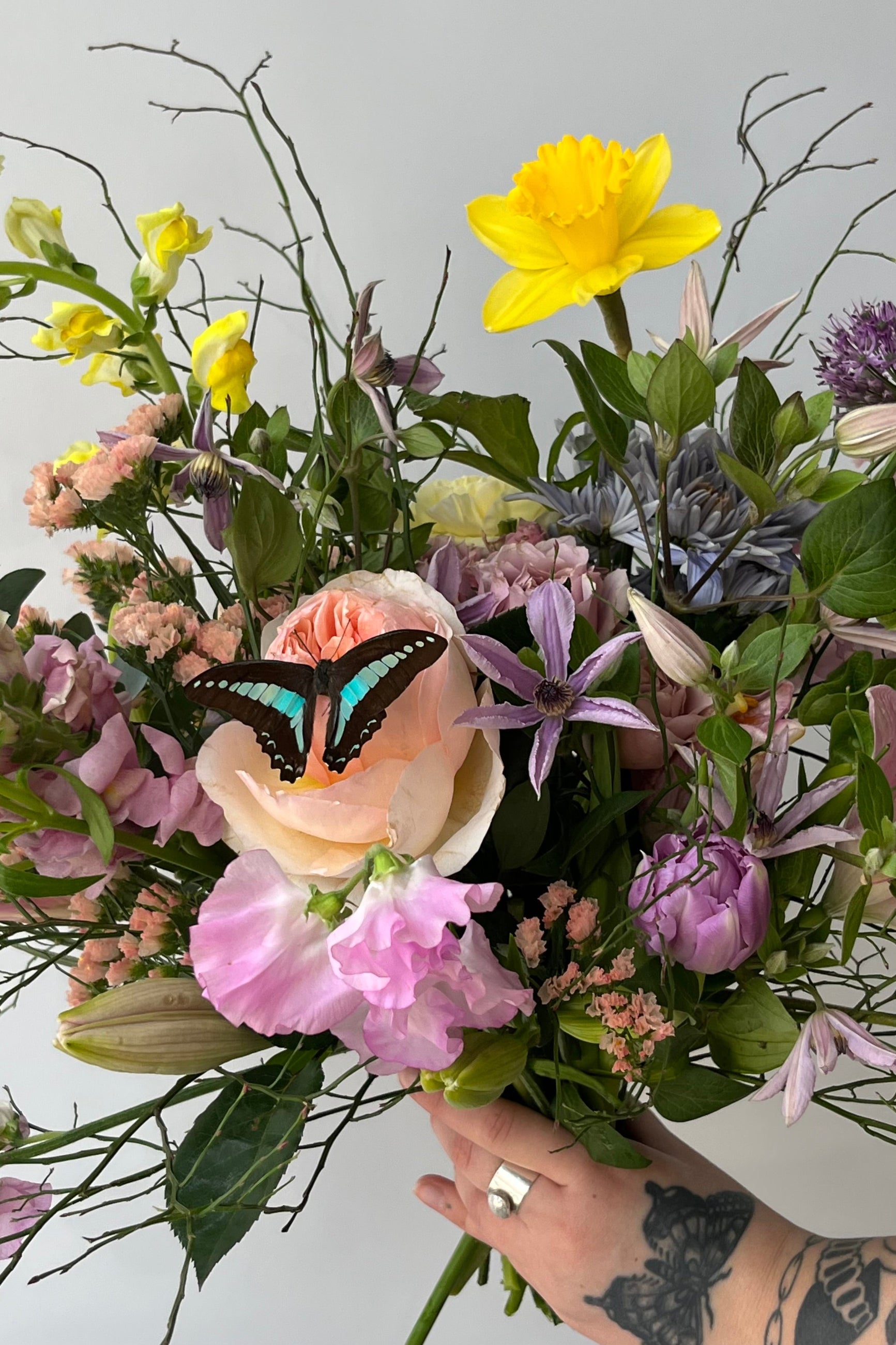 Custom butterflies floral arrangement by Sprout Home being held in hand featuring a aqua and black real butterfly, clematis and sweet pea ©Sprout Home #size_$160