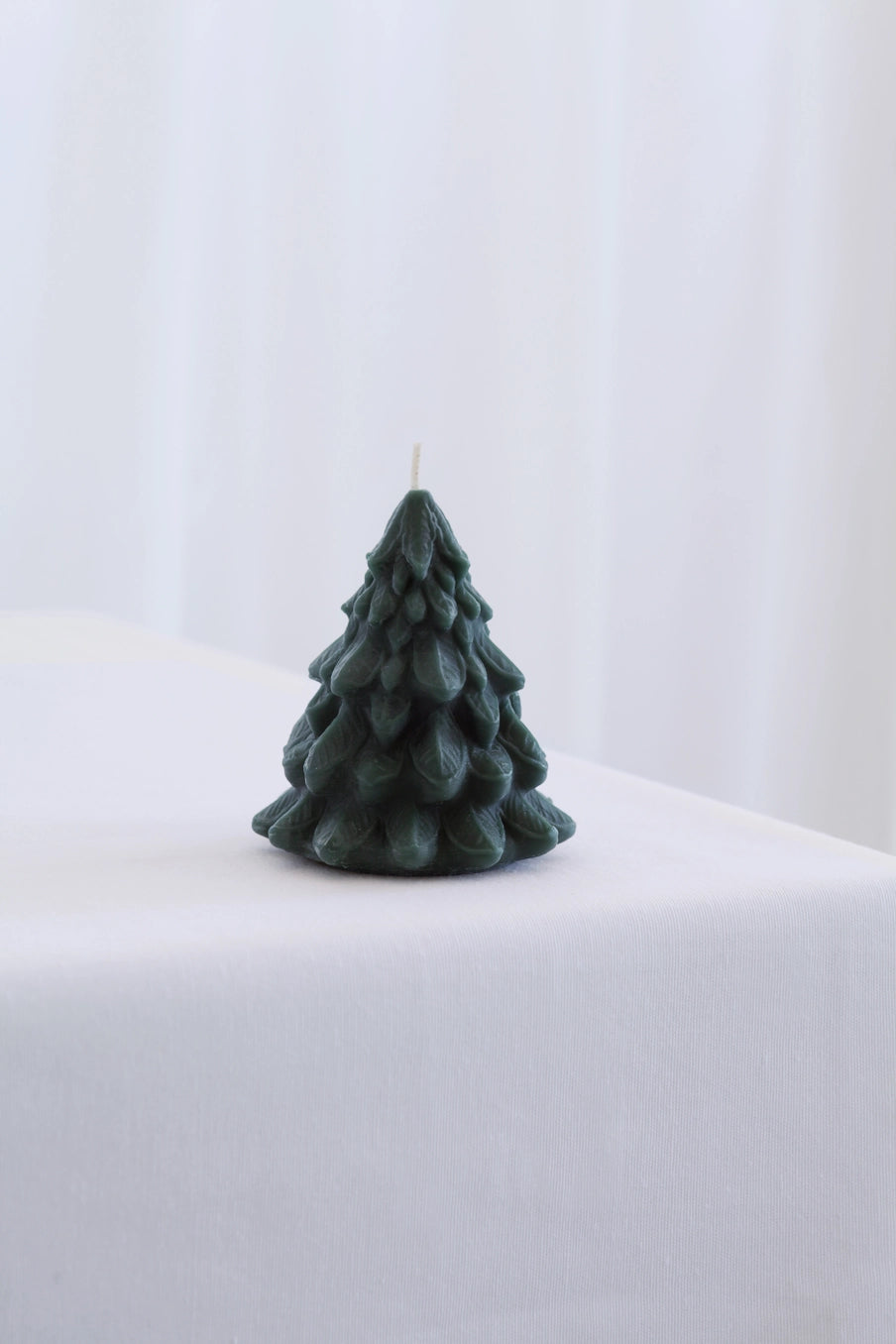 Green tree-shaped candle on a white surface with a white background ©Mo&Co.