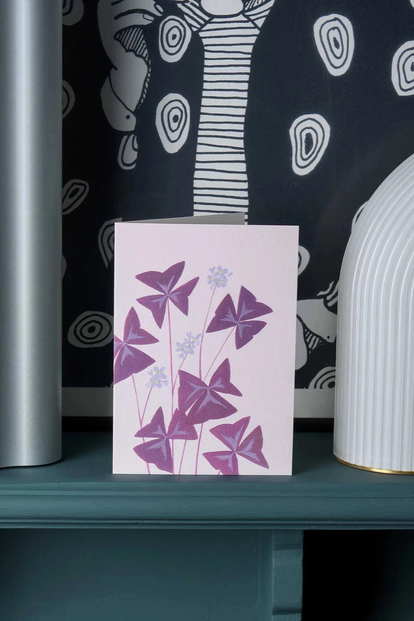 The Oxalix greeting card by Stengun Drawing in a lifestyle shot on a ledge sitting in front of a black and white wall paper.