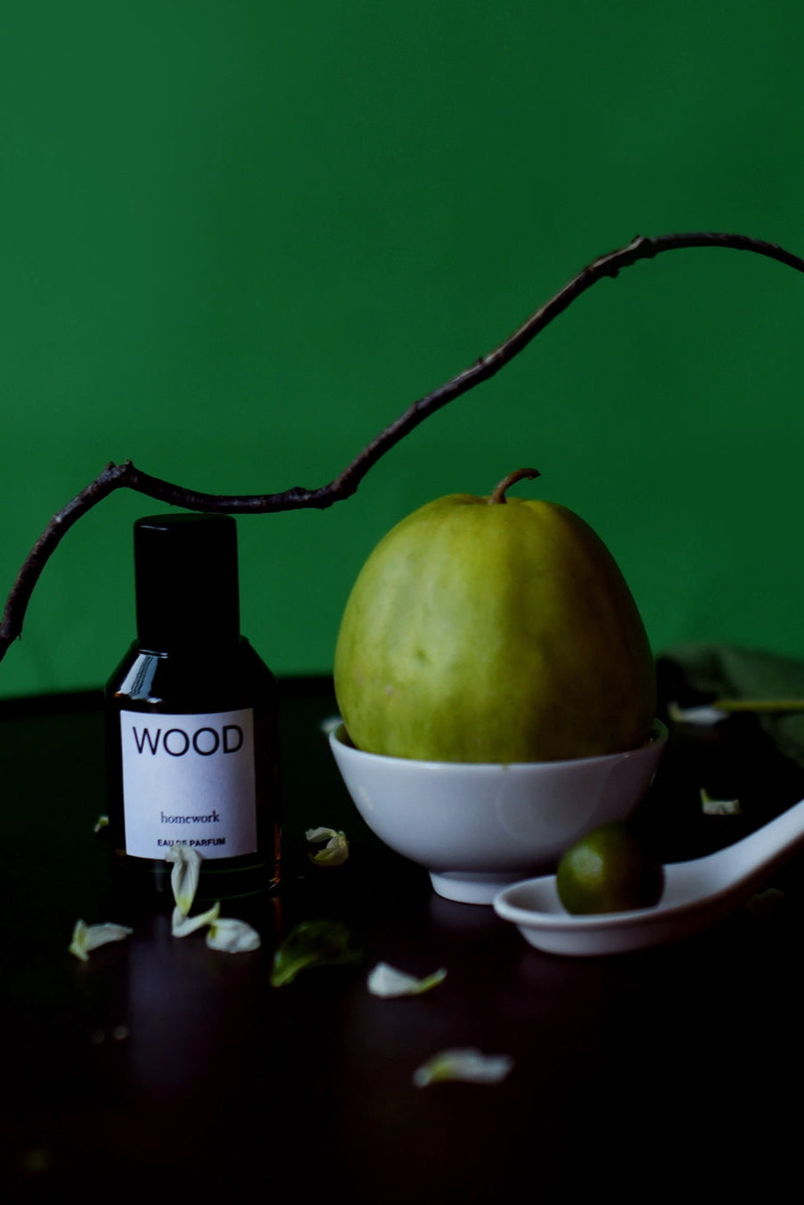 Wood Eau de Parfum Bottle labeled 'WOOD' with a green fruit in a white bowl on a dark surface against a green background ©Homework