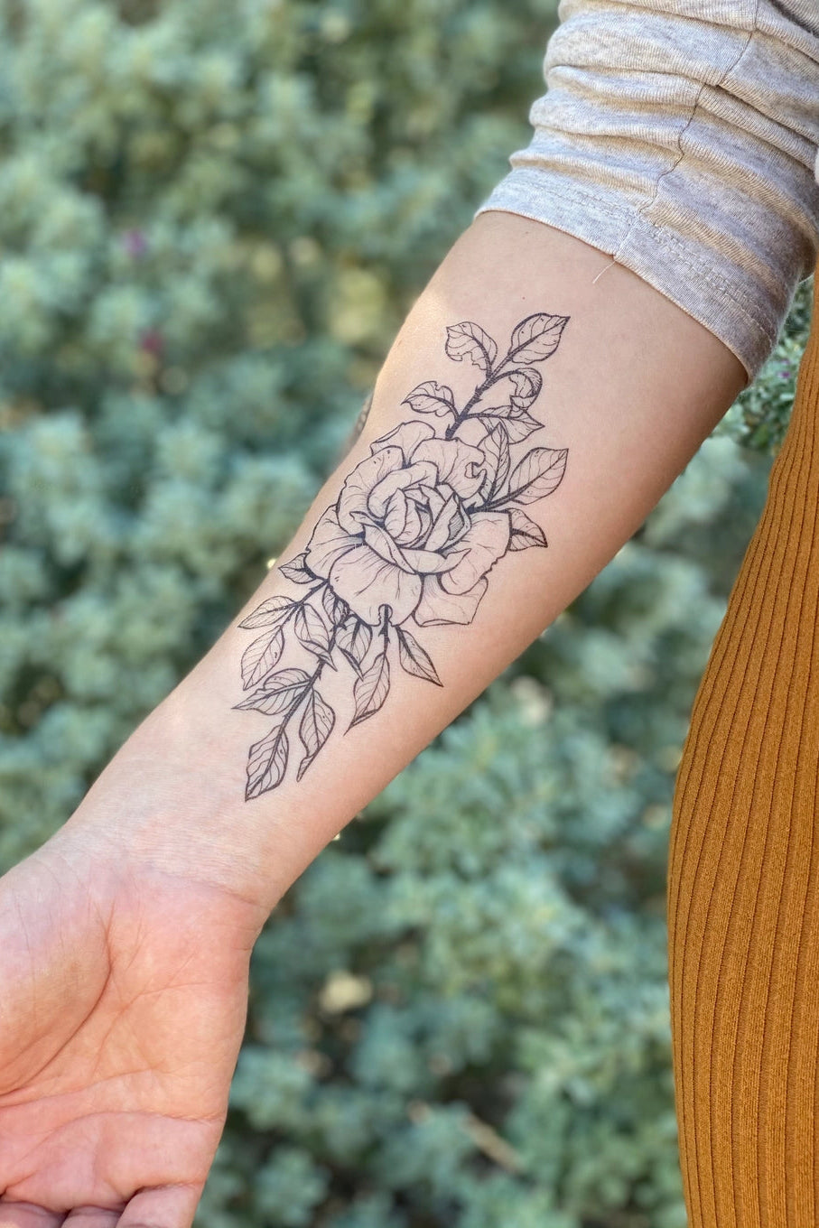 Person with a floral rose tattoo on their arm against a blurred green background ©Nature Tats