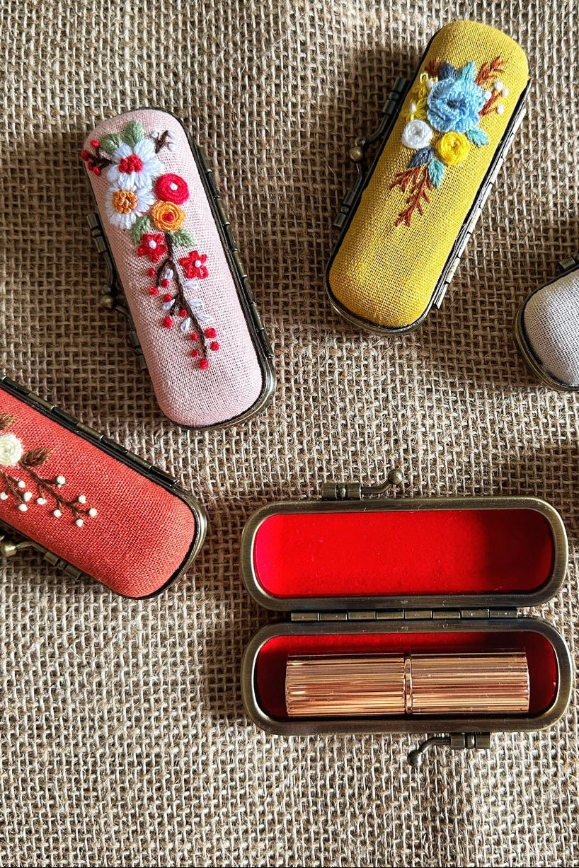Decorative lipstick cases with floral designs on a textured fabric background ©Quince Fables