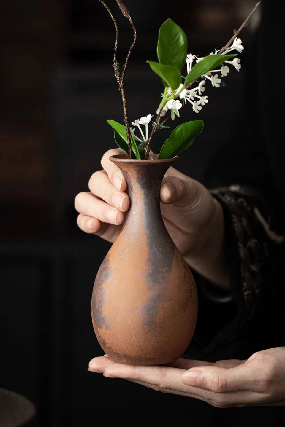 Jade unglazed vase with flowers inside being held in hand ©Haku