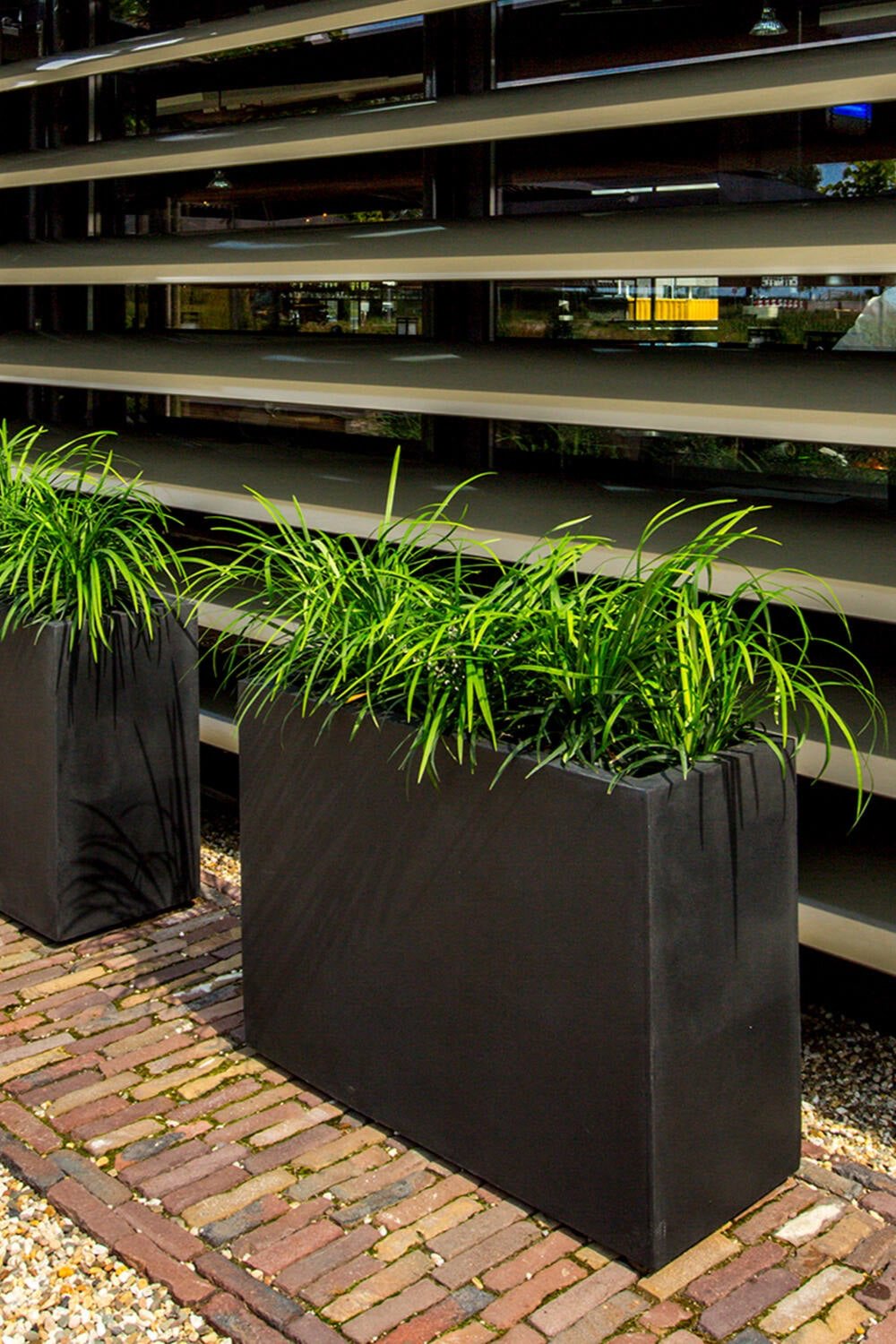 Jort Fiberstone Black Planter filled with Liriope grass on a brick walkway by Pottery Pots