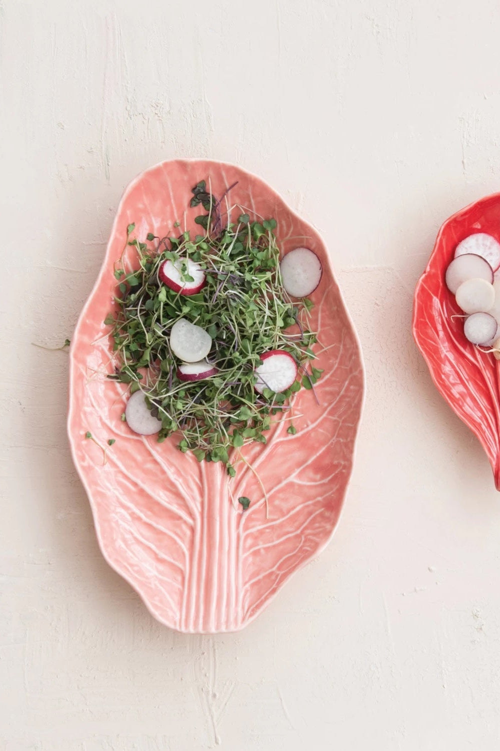 Two leaf-shaped ceramic plates with pink and red glaze holding sliced vegetables on a white surface ©Creative Co-Op)