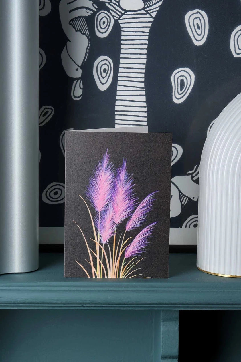 Pink Pampas greeting card by Stengun Drawings in a lifestyle shot on a ledge in front of a black and white wall paper.