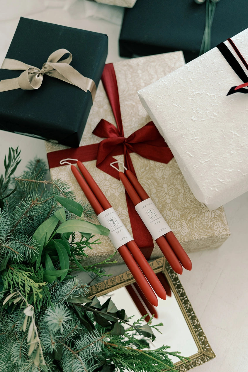 Mo & Co berry red beeswax candles on top of holiday gift wrapped presents.