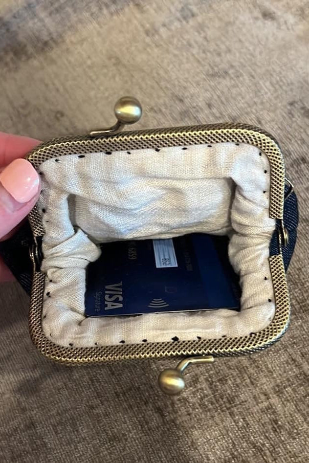 Small clutch purse with a gold clasp held open by a hand on a textured surface ©Quince Fables