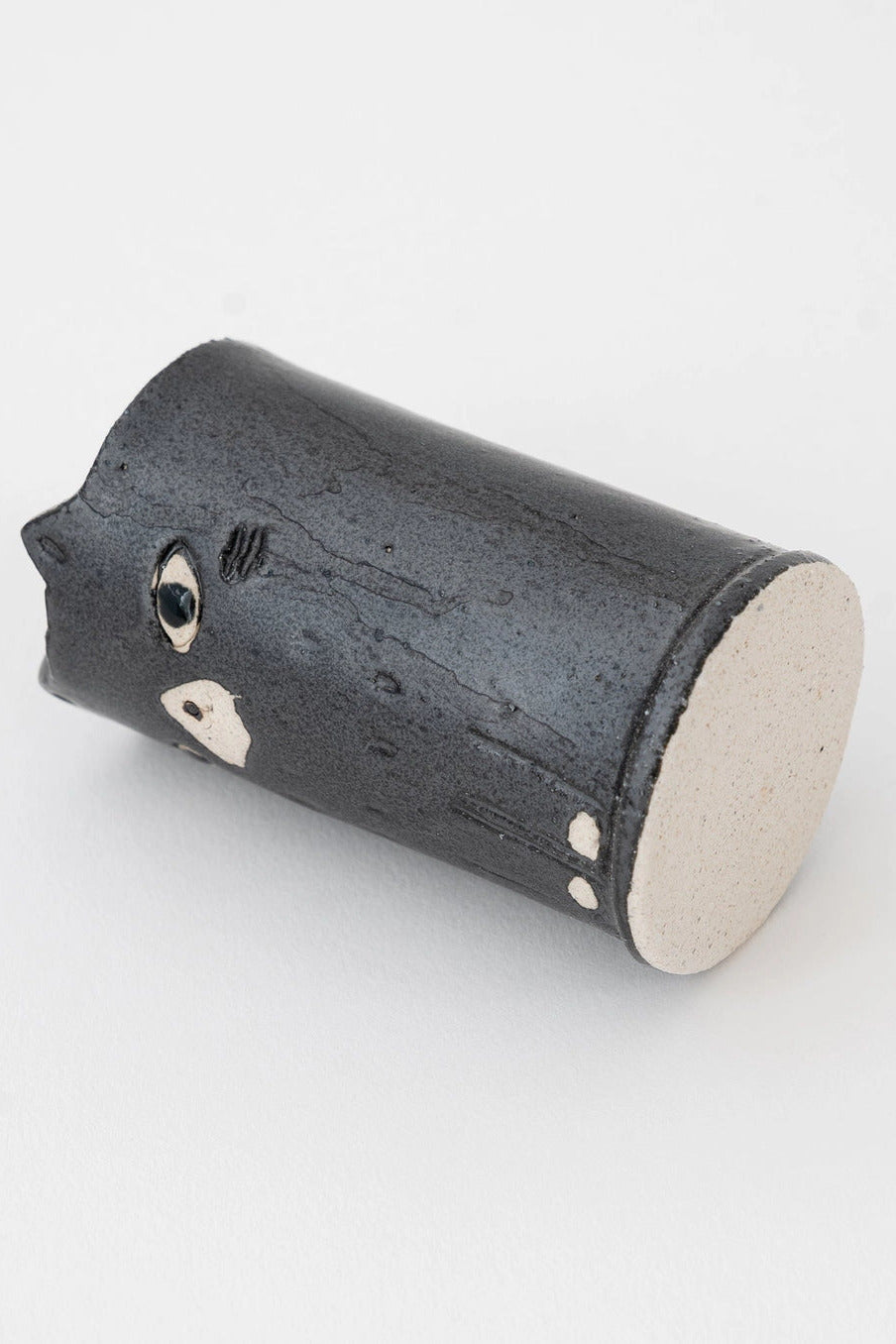 A small handmade ceramic cat vase with a dark charcoal black exterior and a light beige interior, featuring a stylized face with a single visible eye and small white speckles, photographed on a clean white background. ©Great Zakka