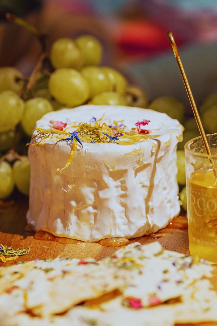 Cheese platter with honey, crackers, and grapes with edible flower petals on a wooden board. ©Flouwer Co.