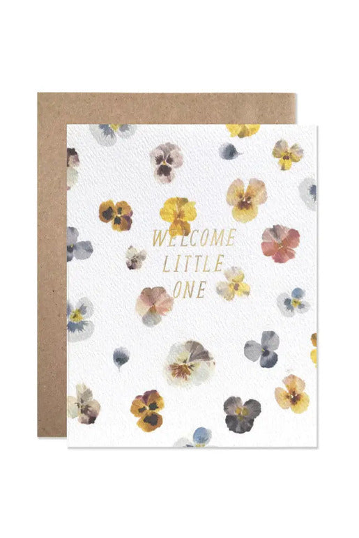 Welcome Little One By Helen Dealtry Card with a watercolor floral pattern in muted yellow, pink, blue, and brown tones, featuring the words 'WELCOME LITTLE ONE' in gold foil lettering, shown with a brown kraft envelope behind it on a white background. ©Hartland Cards