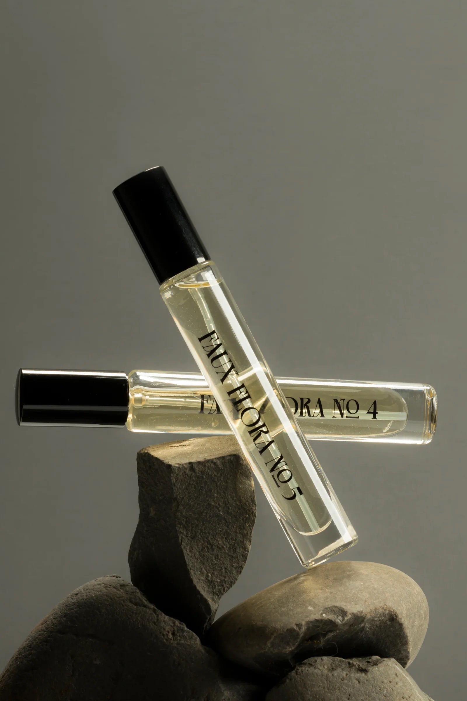 Two small perfume bottles with black caps held by a gloved hand against a gray background ©Fischersund