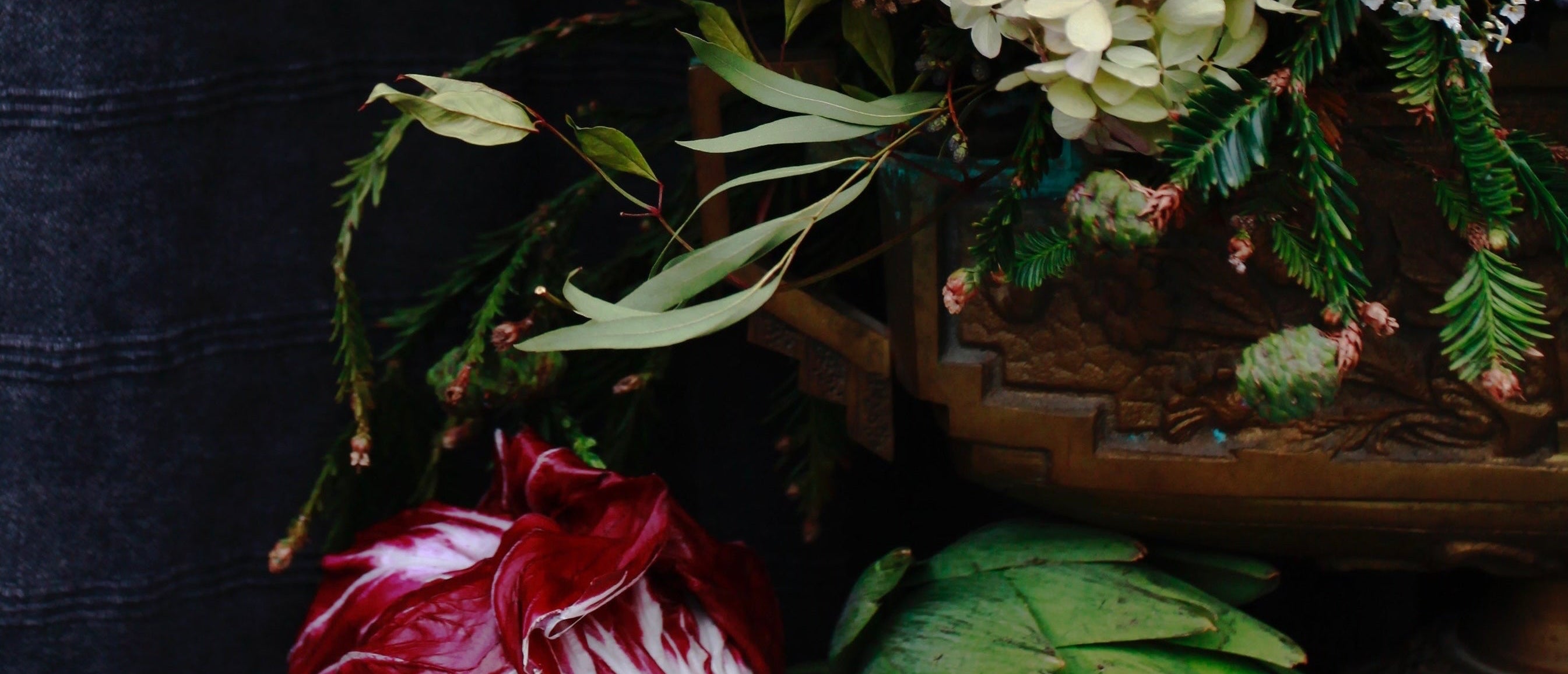 Close-up of a floral arrangement with artichokes on a textured surface.