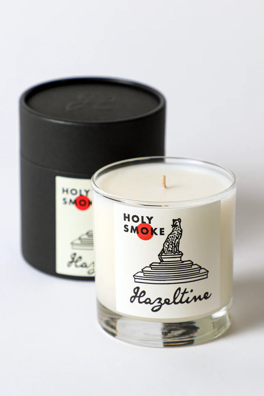Candle with 'Holy Smoke' label and black cylindrical container on a light gray background ©Hazeltine