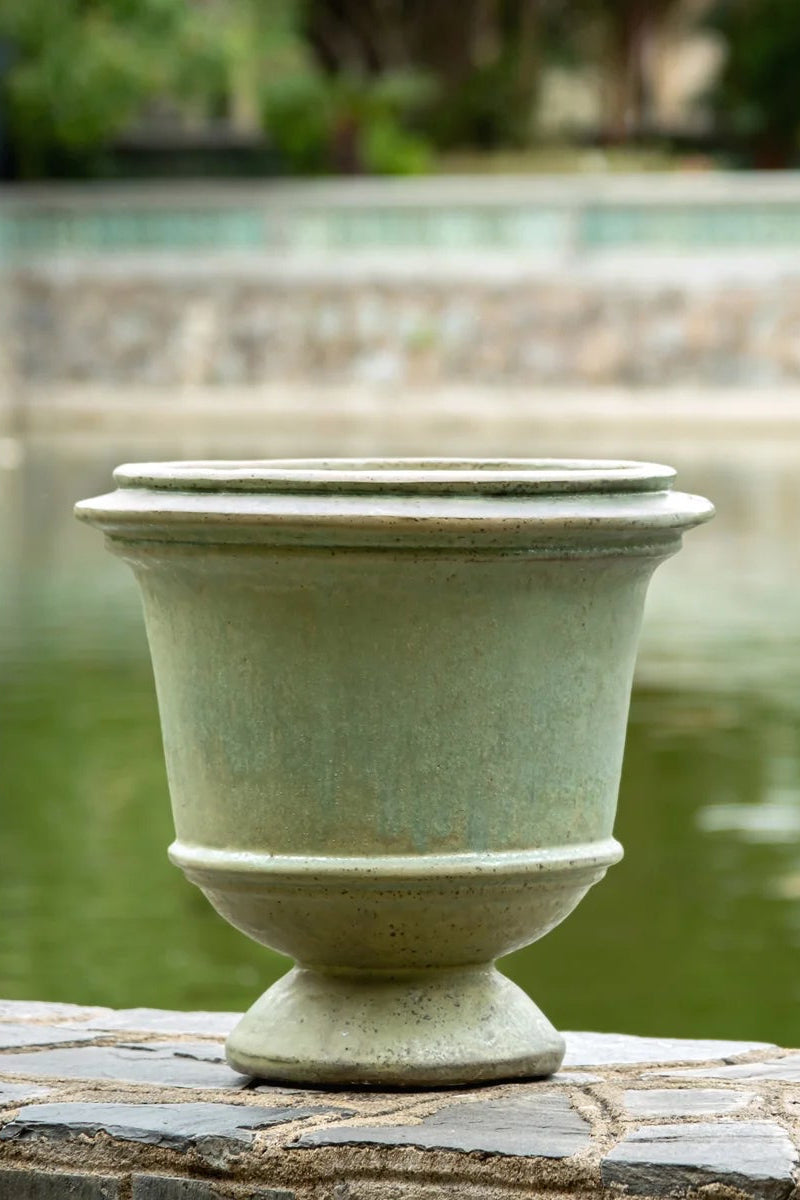 Decorative urn on a stone ledge by a pond with blurred greenery in the background ©Amamese