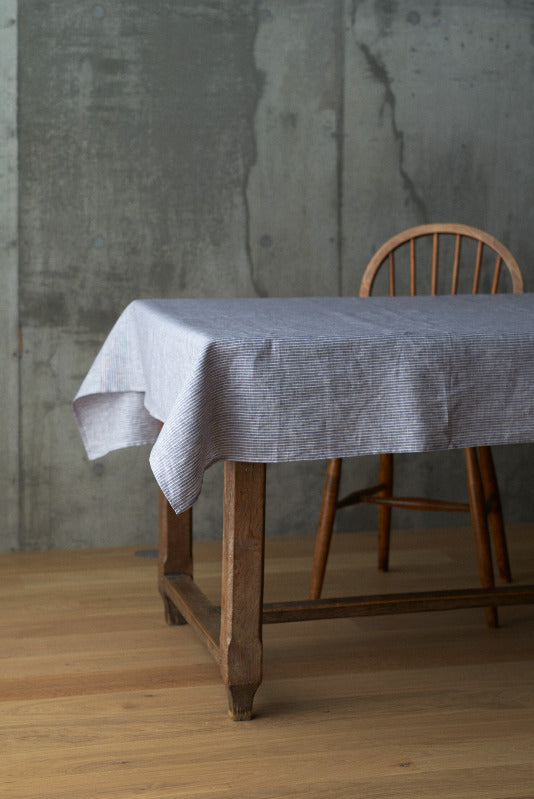 Grey and white striped tablecloth on a wood farm table on a wood floor and a concrete wall.