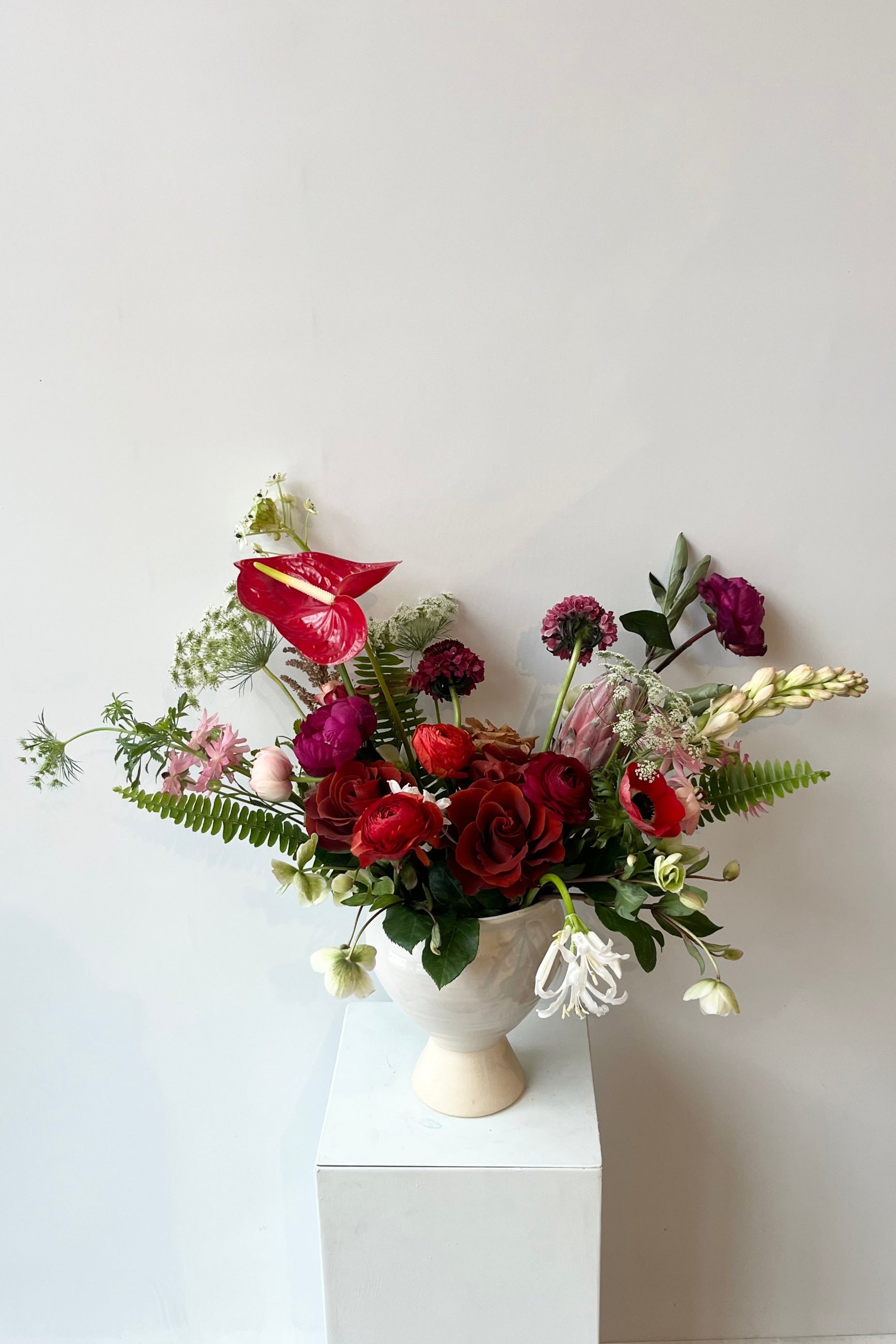 A custom floral arrangement by Sprout Home featuring red anthurium and red roses in a white compote ©Sprout Home #size_$200