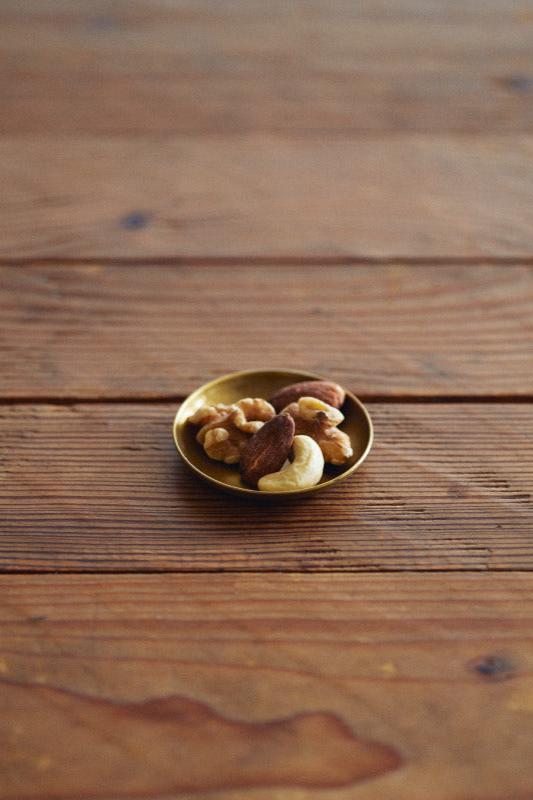 The extra extra small Fog Linen Work brass plate holding some nuts on a wooden table.