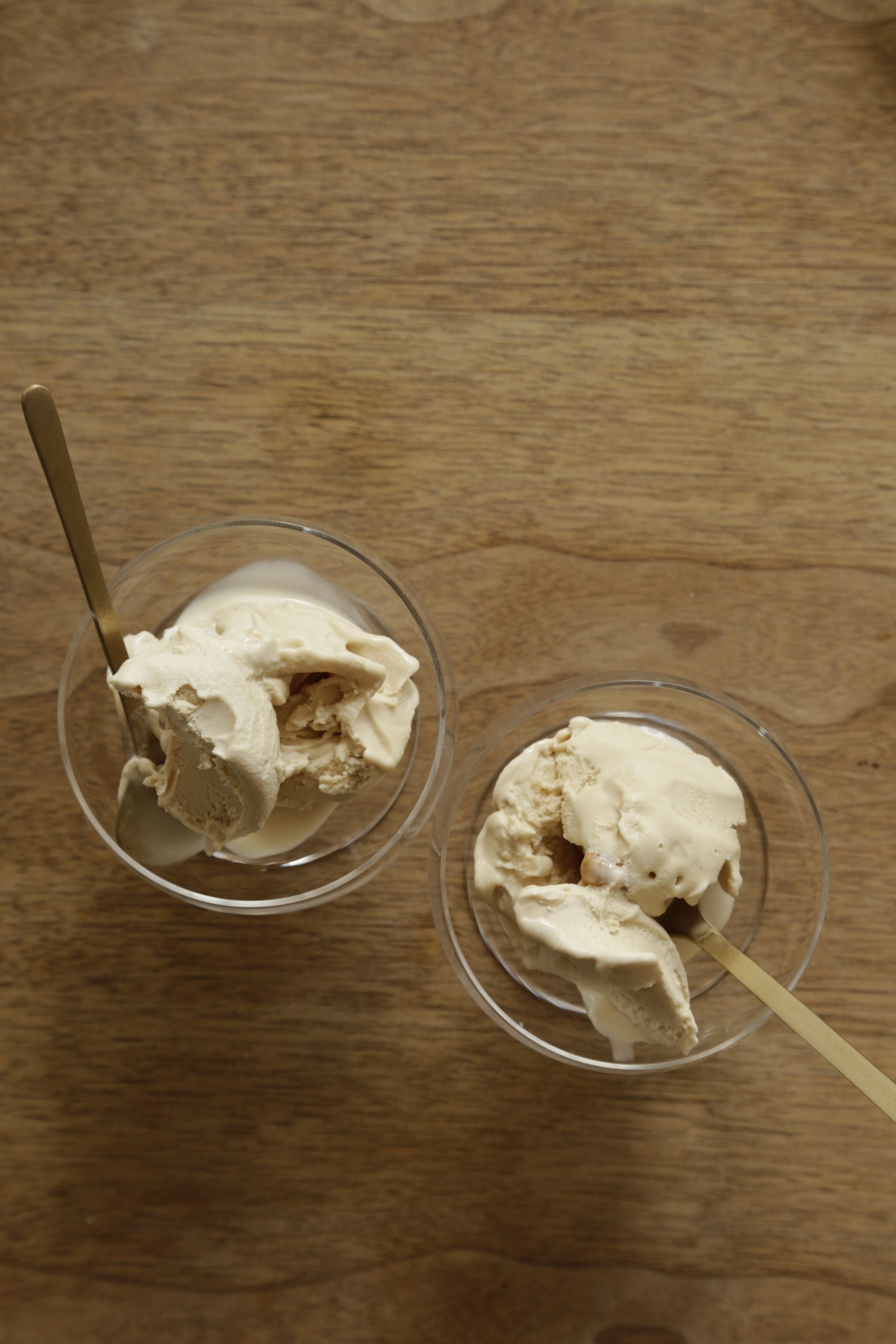 Two bowls of ice cream on a wood surface looking into the bowls and each bowl has a brass dessert spoon by Fog Linen Work.