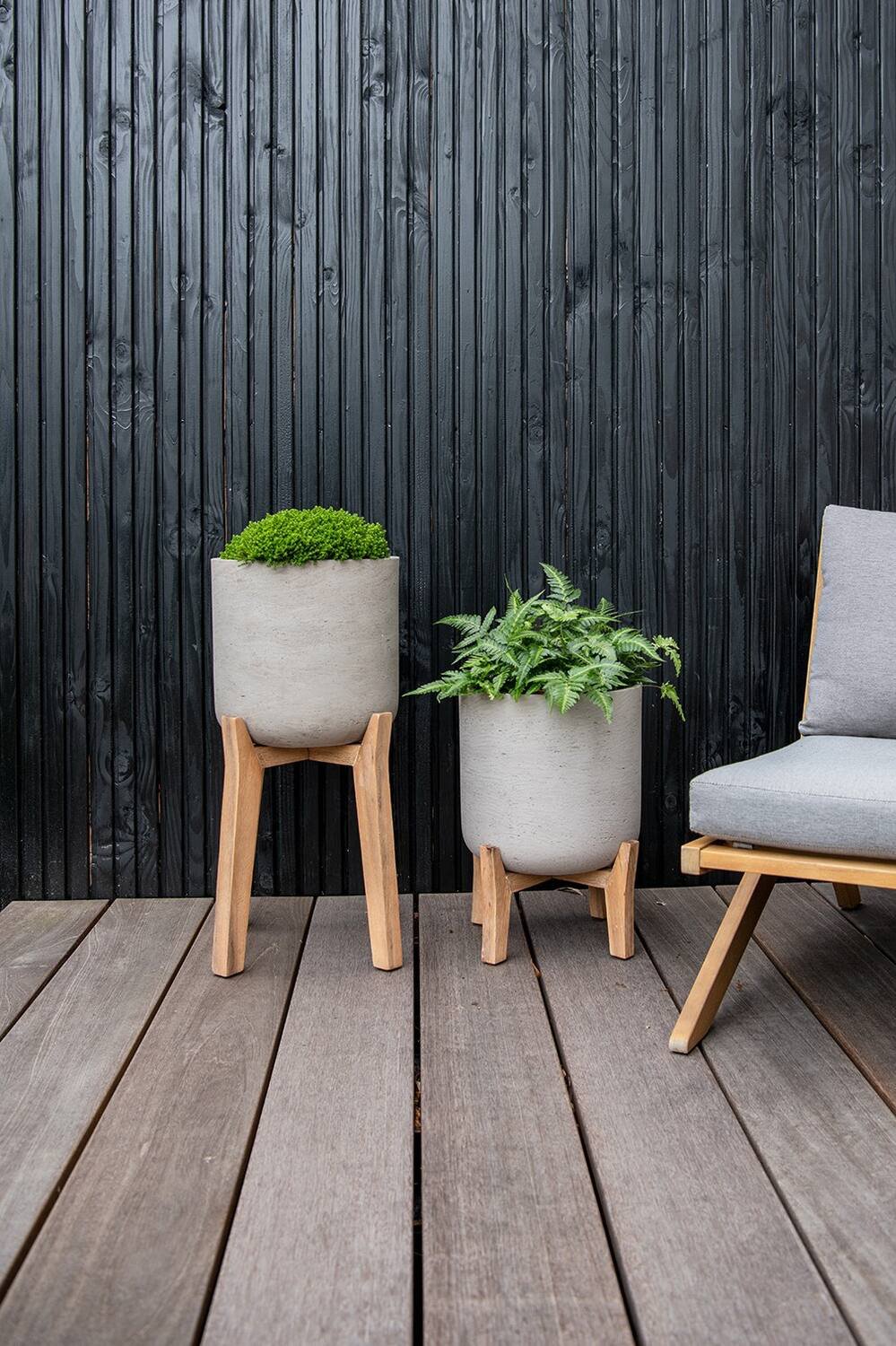 two sizes of Grey Charlie Pot on Stand by Pottery Pots on a deck in front of a black slatted wood wall.