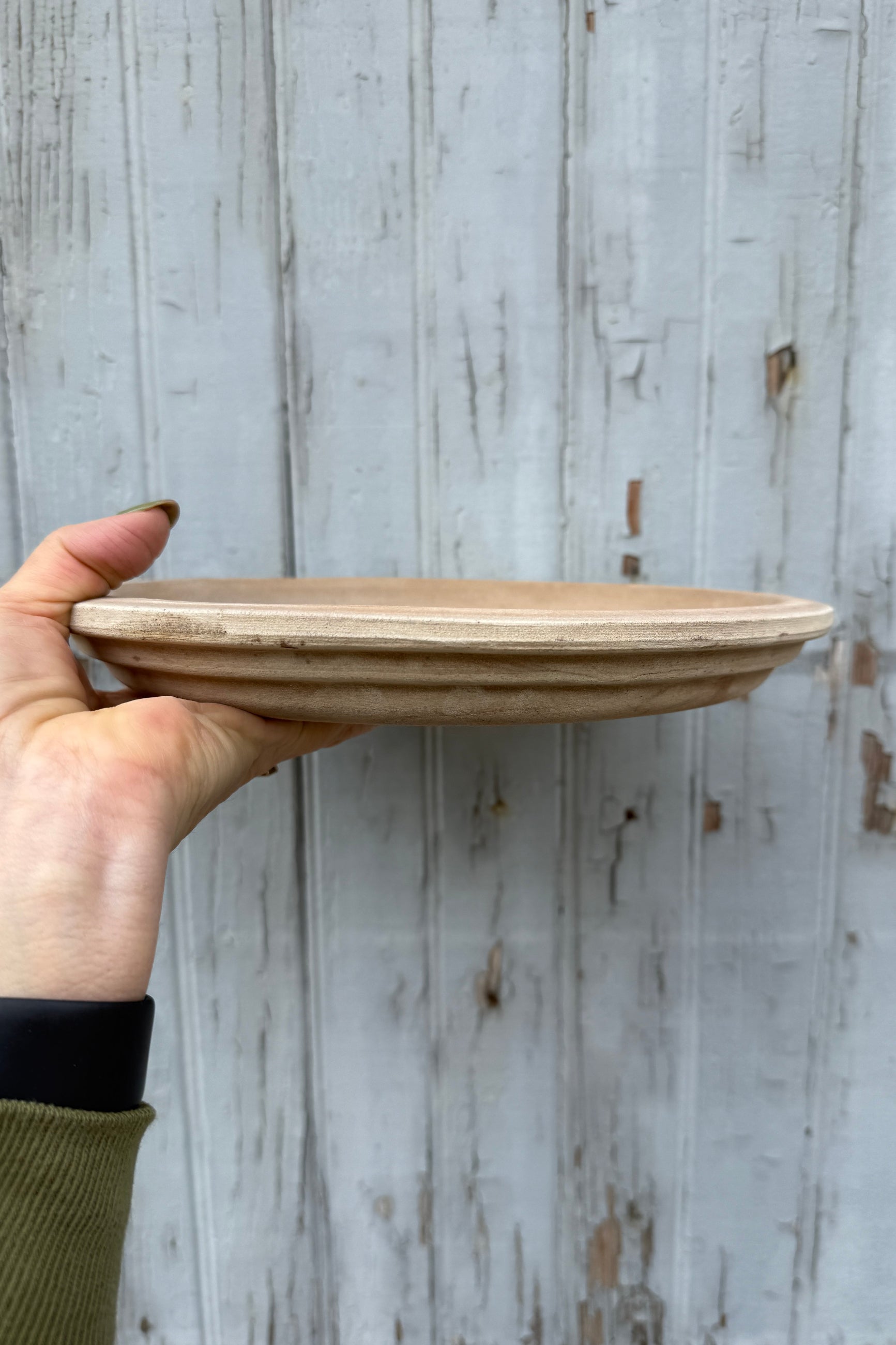 Round Vietnamese Unglazed 11" Saucer being held in hand and shown at eye level from the side ©Sprout Home