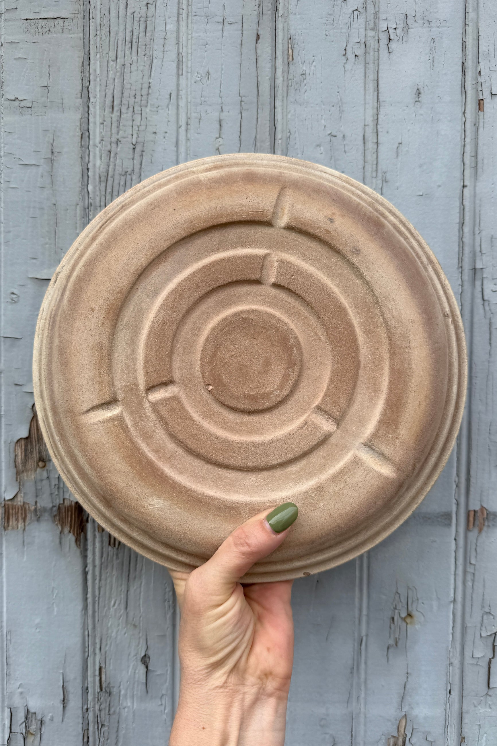 Hand holding a round, textured ceramic plate showing the bottom against a rustic wooden background ©Sprout Home