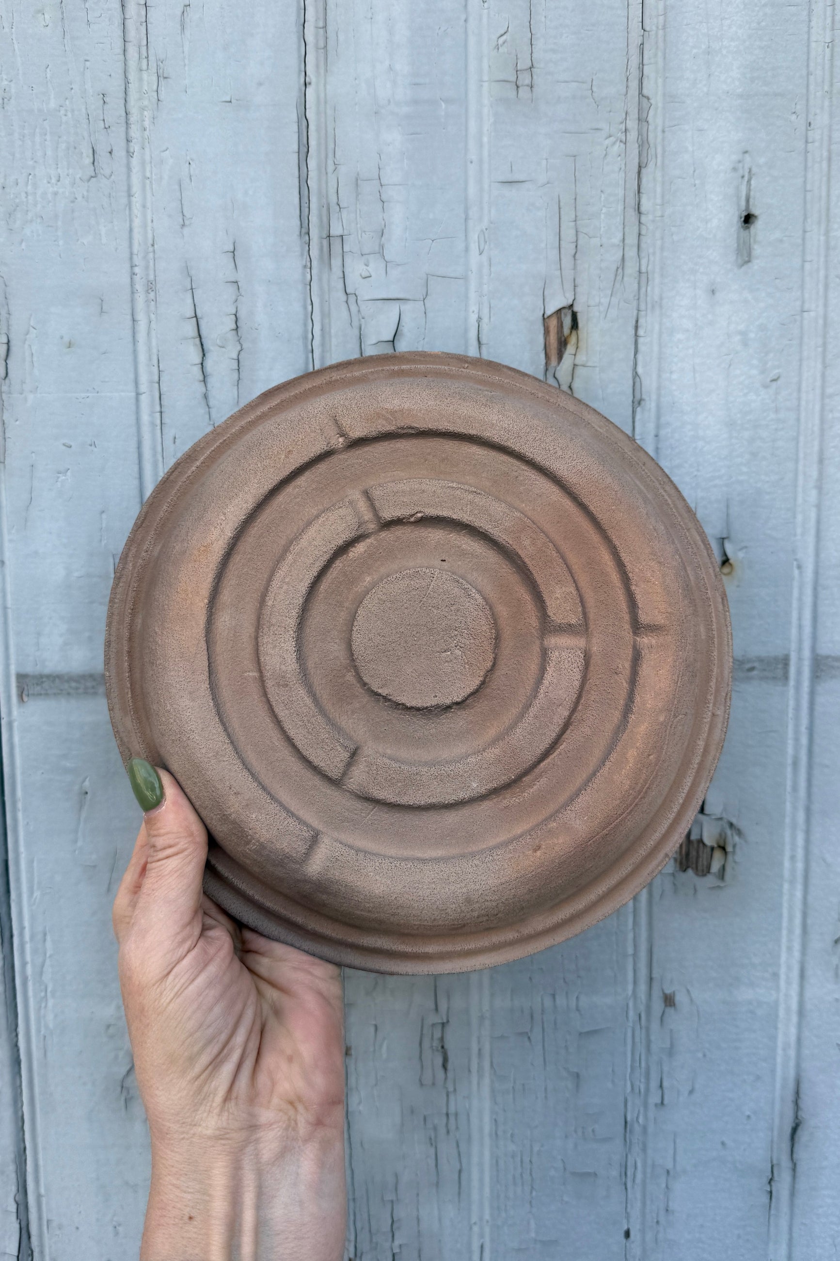 Hand holding a terracotta saucer against a wooden background ©Sprout Home