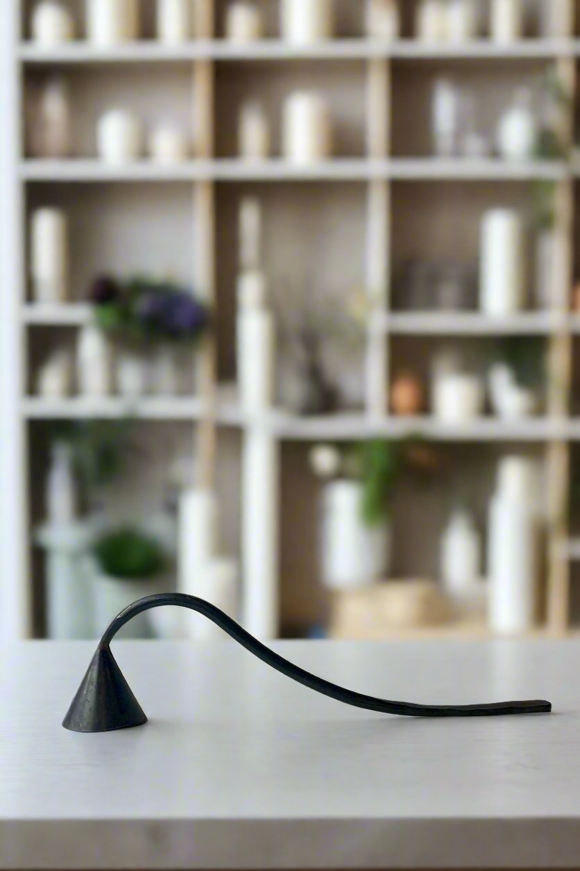 Black iron candle stuffer on a white table in front of a wall of candles to light. ©Sprout Home