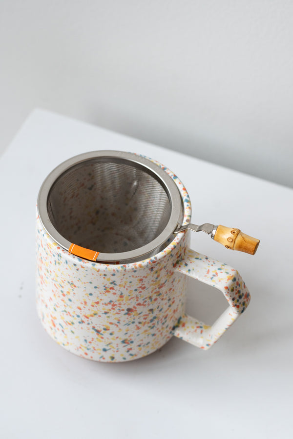 Stainless steel tea strainer by Miya sits in a speckled mug on a white surface in a white room