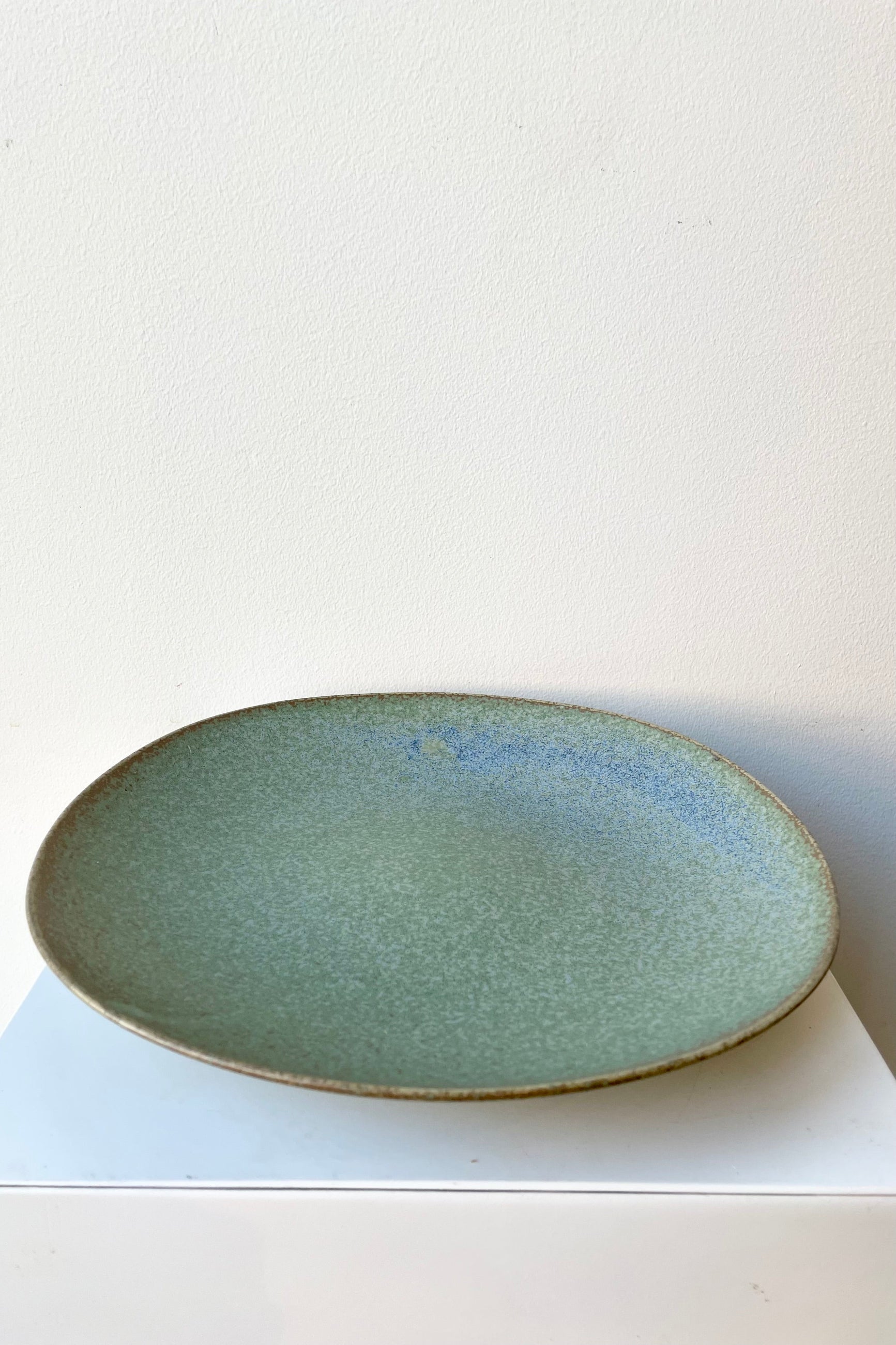 The Shiho plate in terra green against a white wall sitting on a white pedestal. ©Sprout Home
