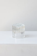Clear pleated glass taper candle holder sits on a white surface in a white room