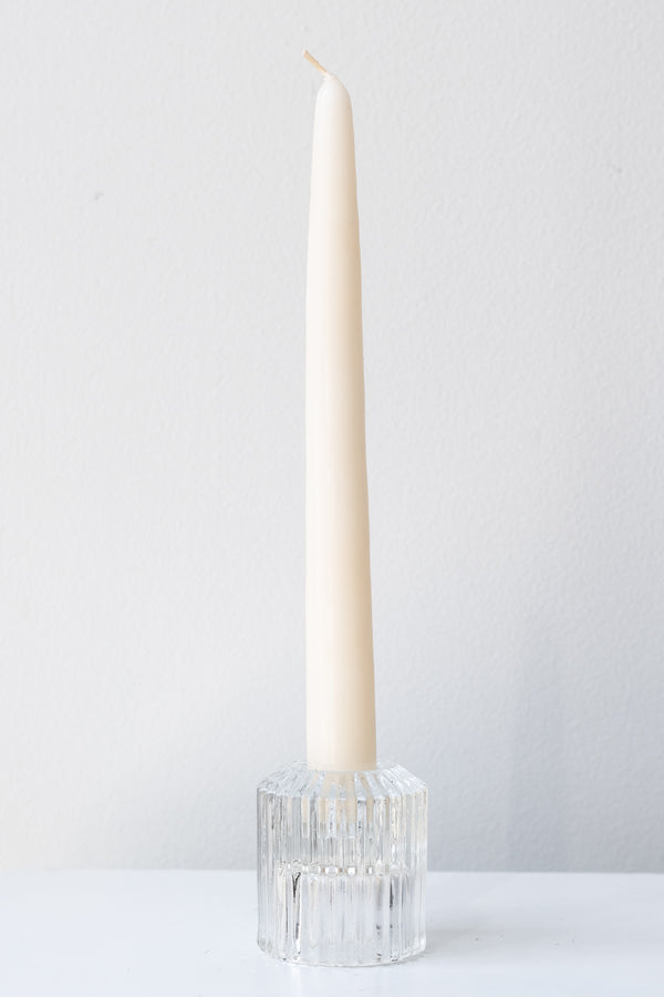White taper candle inside clear pleated glass candle holder in front of white background