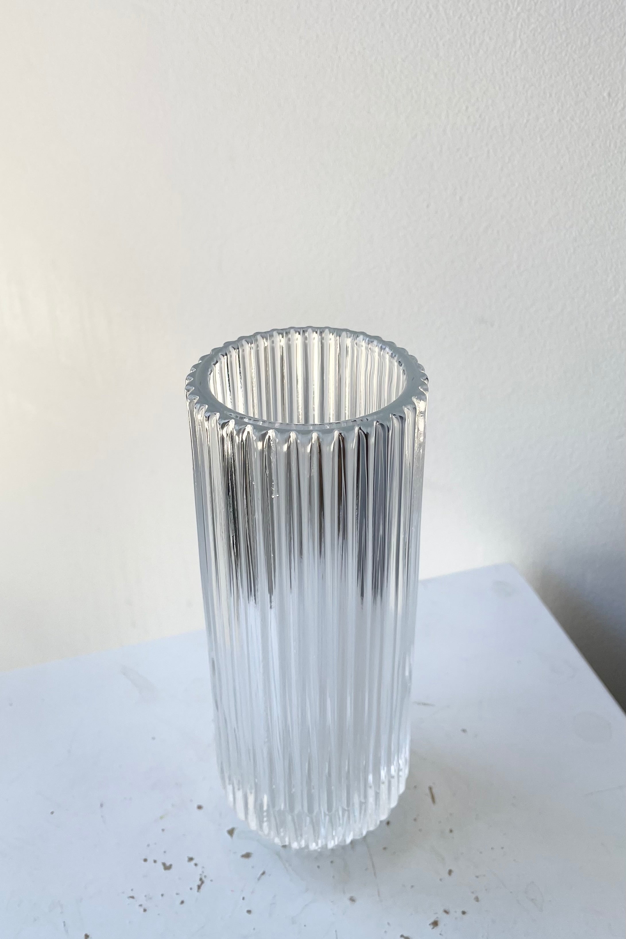 The 6 1/4" pleated clear glass vase against a white wall at Sprout Home.