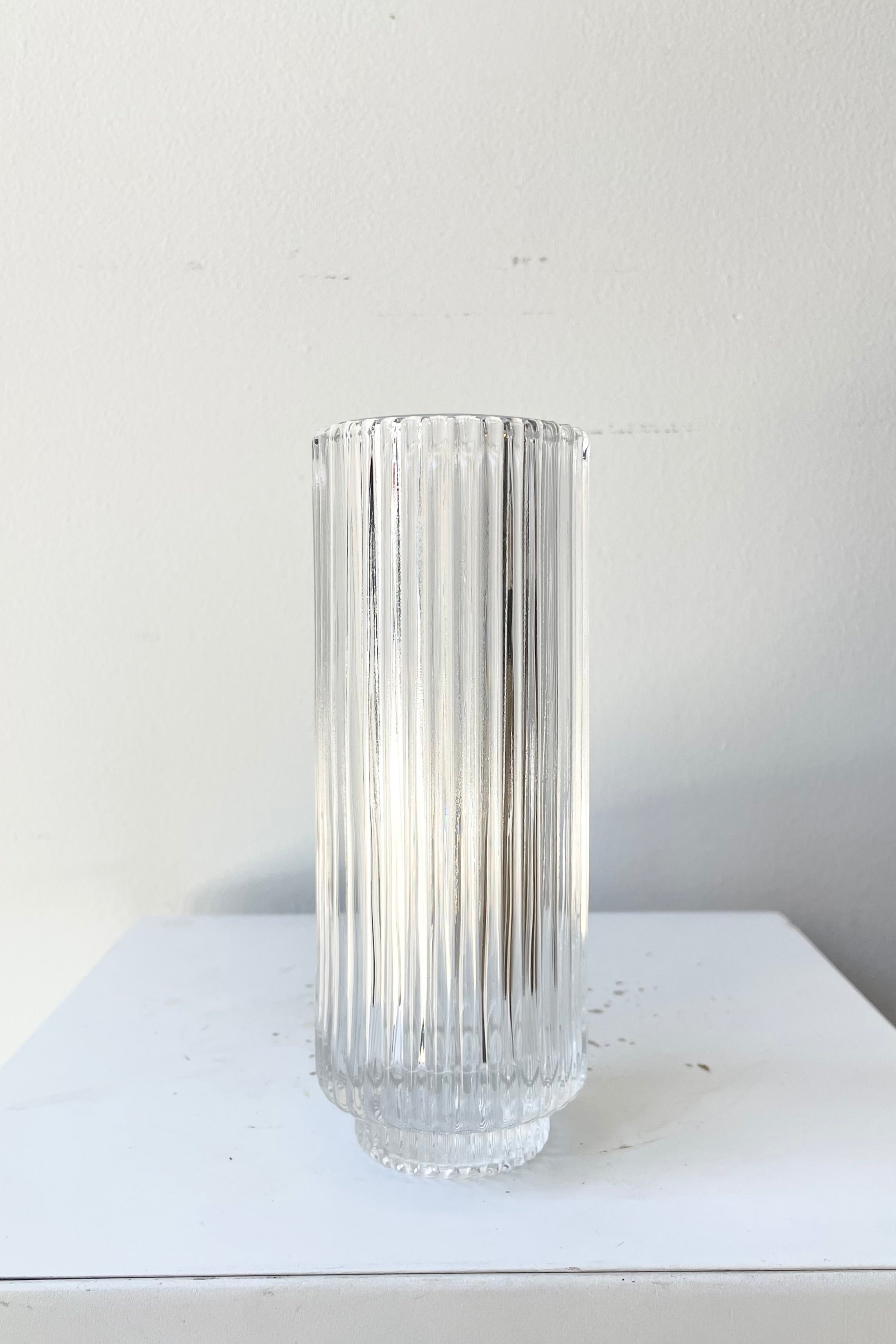 The 6 1/4" pleated clear glass vase against a white wall at Sprout Home.