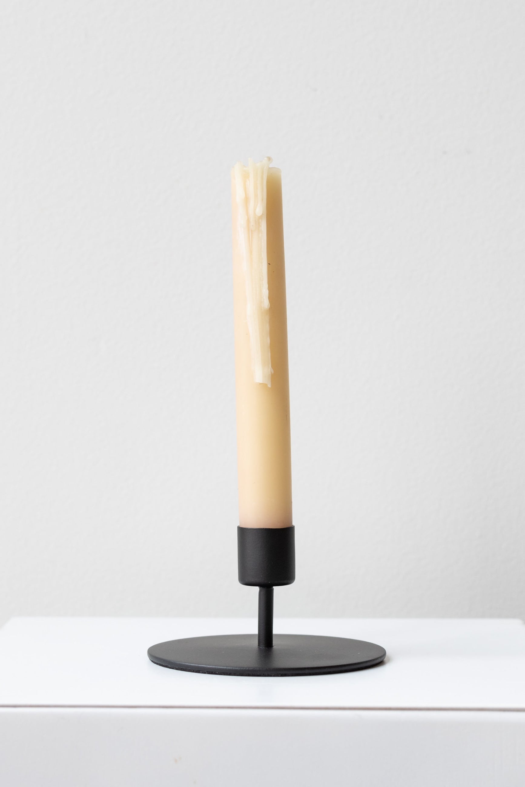 Short black Kent candlestick holder with a neutral taper candle inside slightly dripping ©Sprout Home