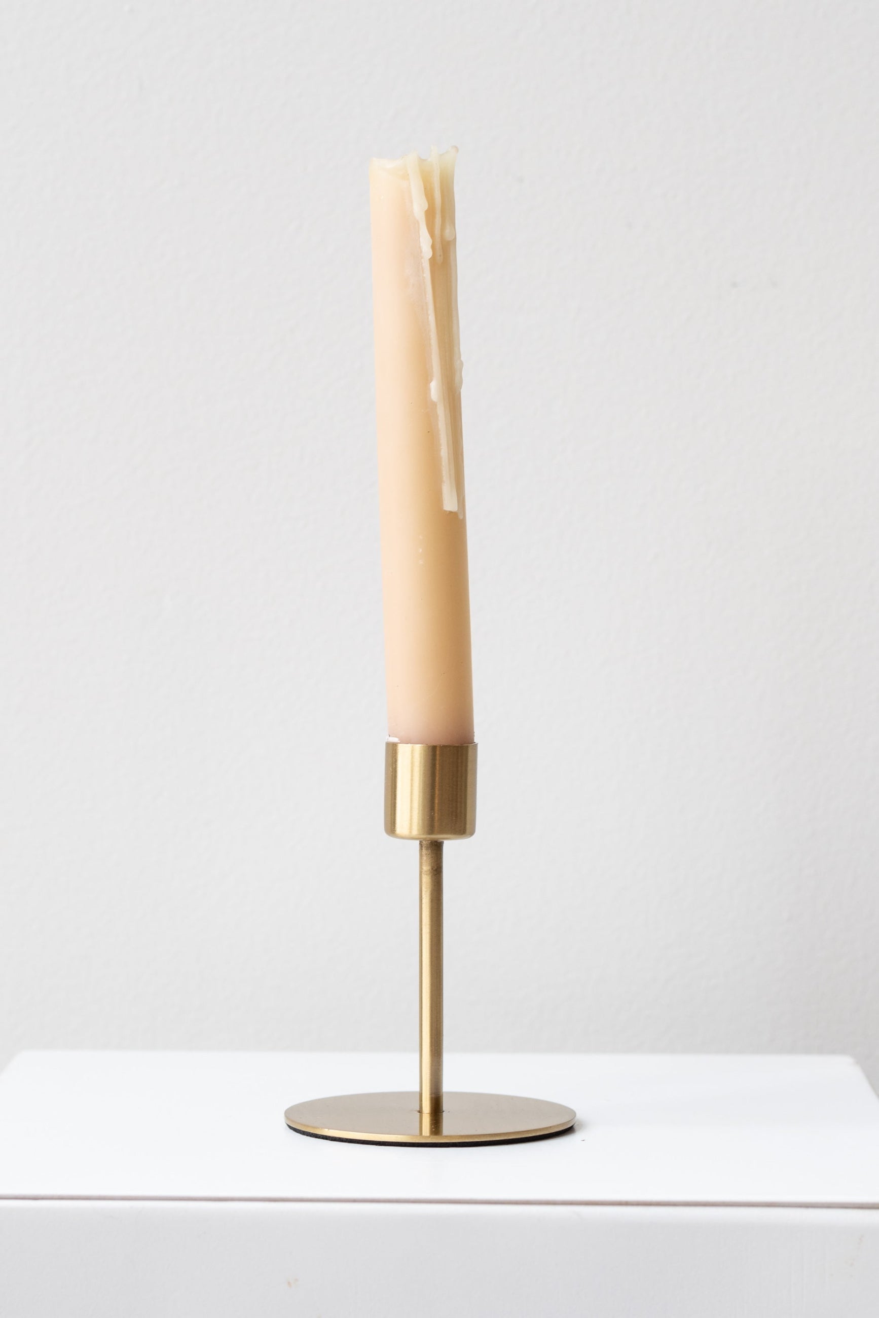 Kent medium gold taper candle holder with a natural colored taper candle inside with it slightly dripping ©Sprout Home