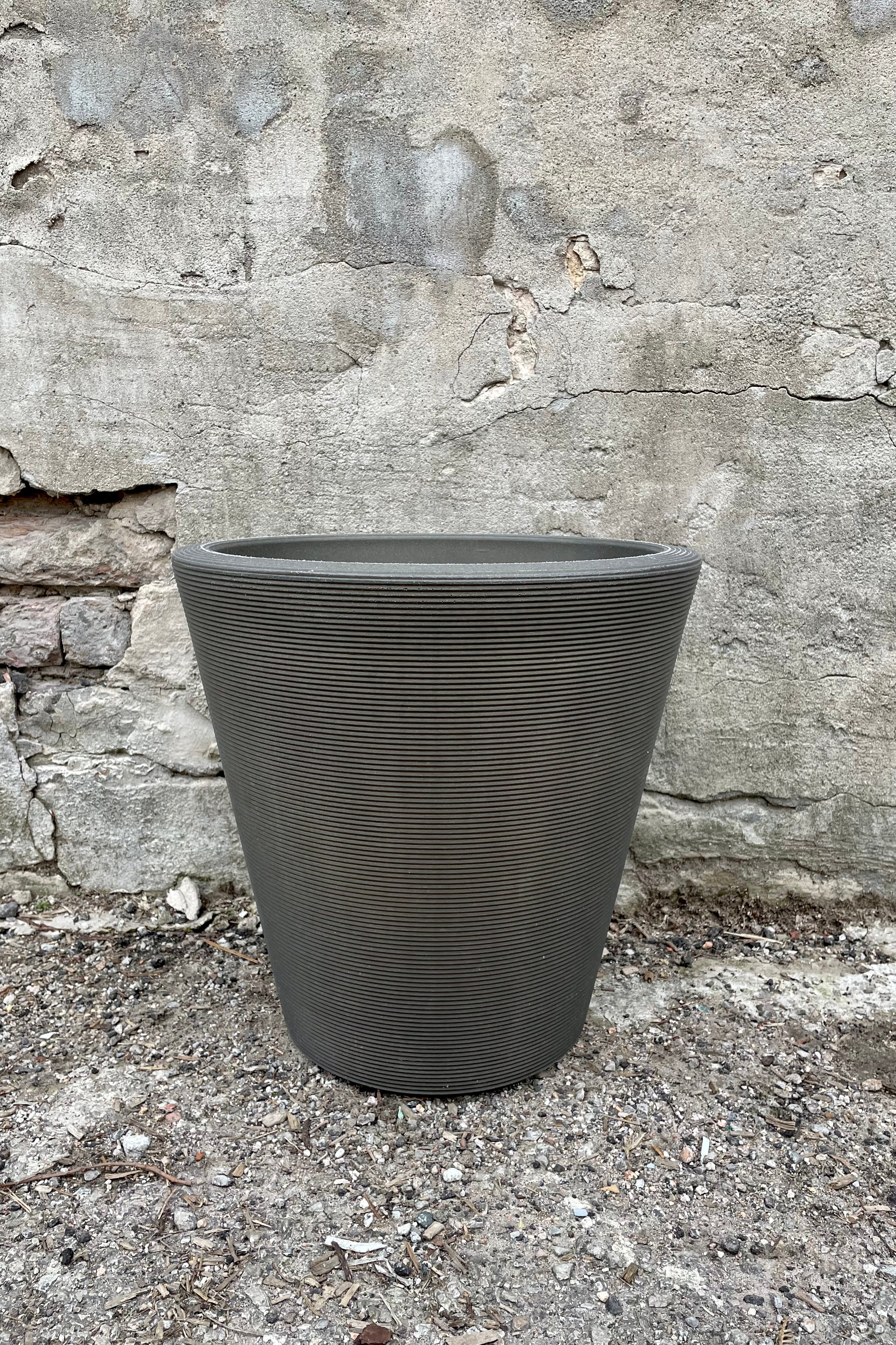 The 14" old bronze madison planter against a cement wall.