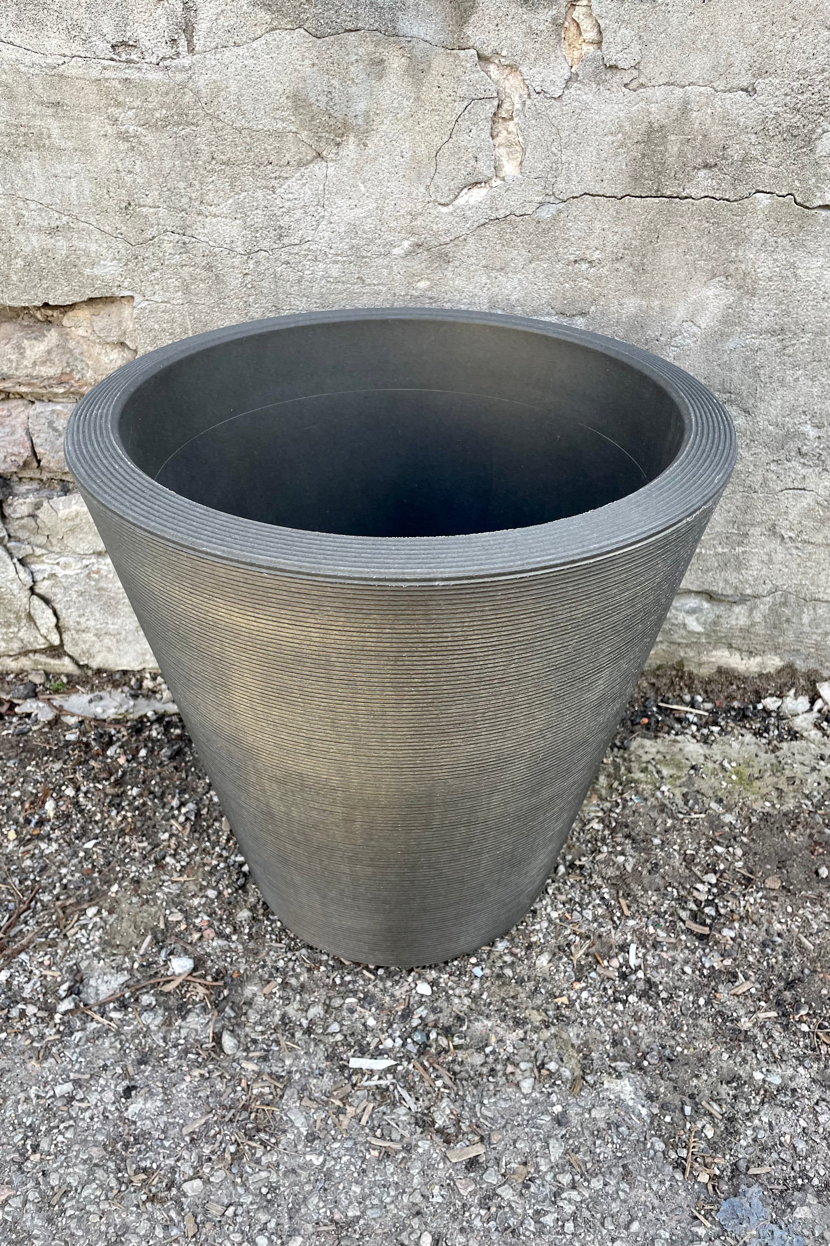 The 16" old bronze madison planter shown from the side and above against a concrete wall.