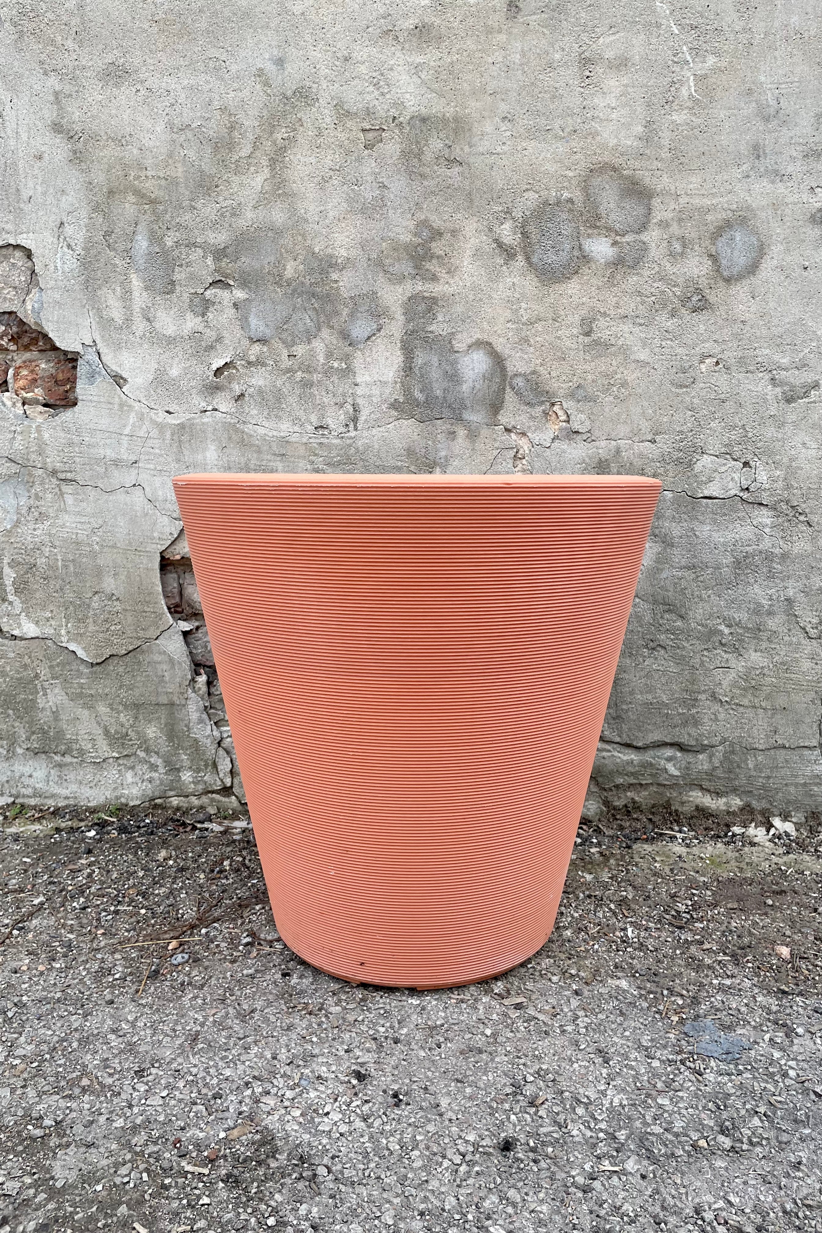 The weathered terracotta madison 20" container against a concrete wall.