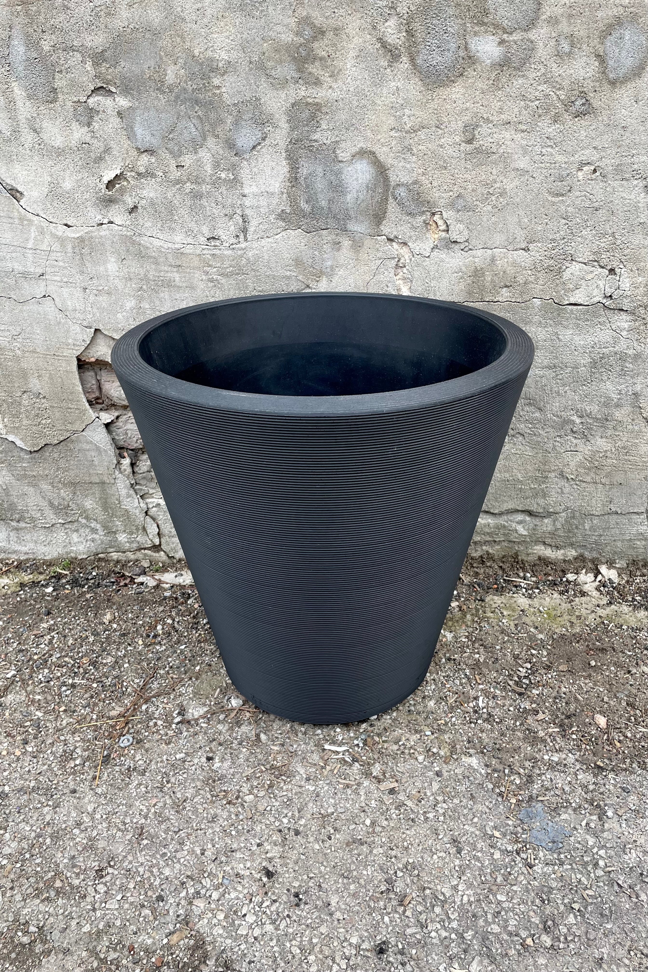 The outdoor Madison 20" planter in caviar black against a cement wall.