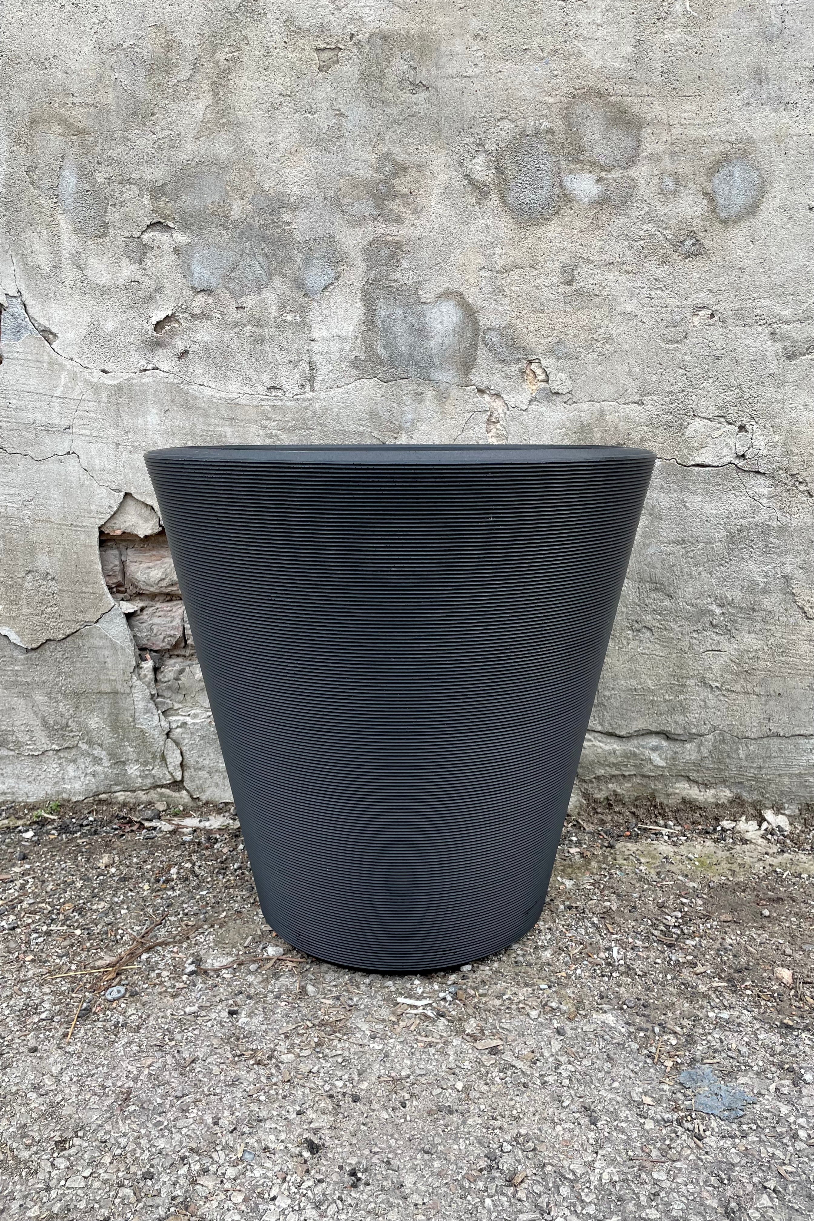 The outdoor Madison 20" planter in caviar black against a cement wall.