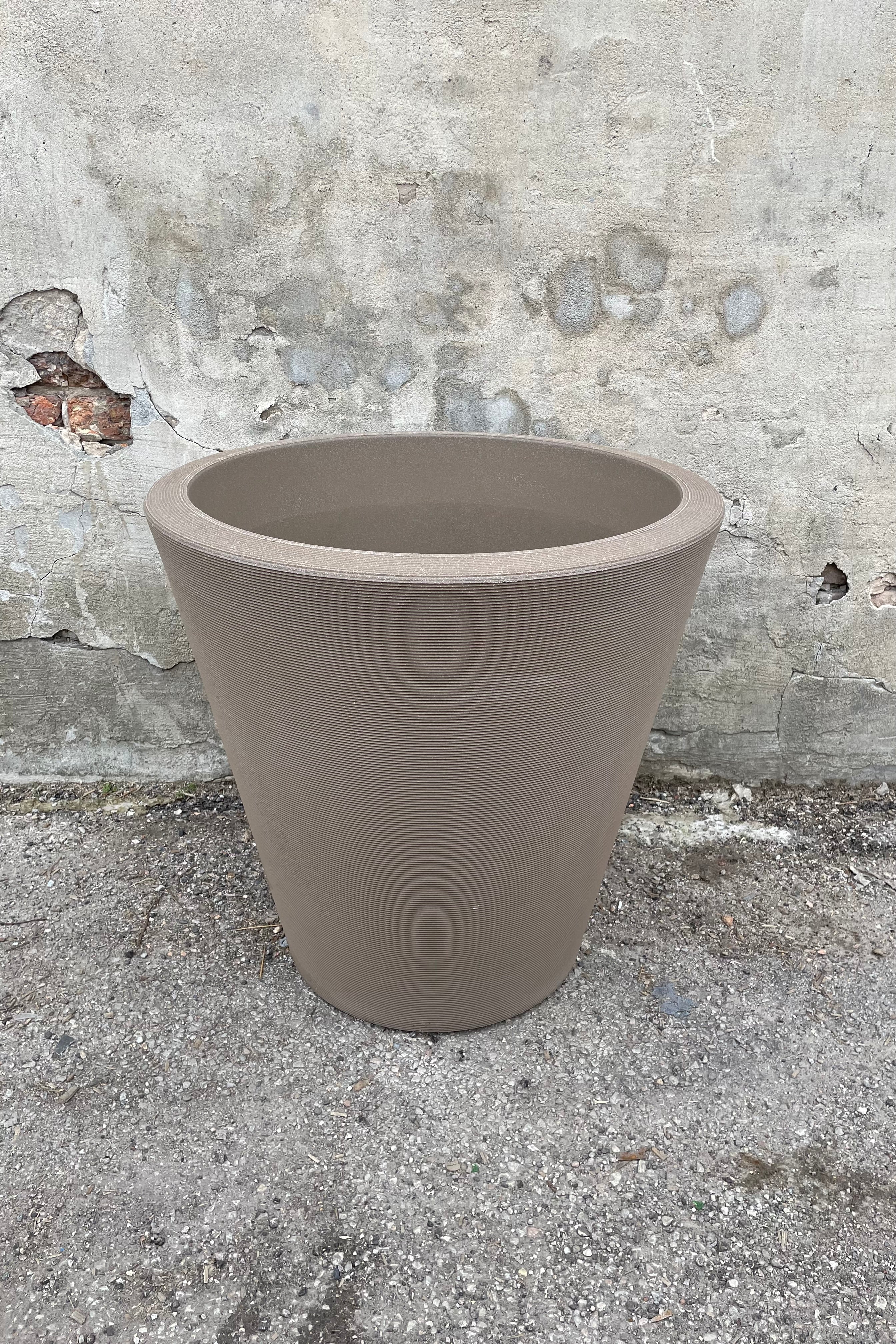 The 26" mocha Madison planter shown from the front and top against against a concrete wall.