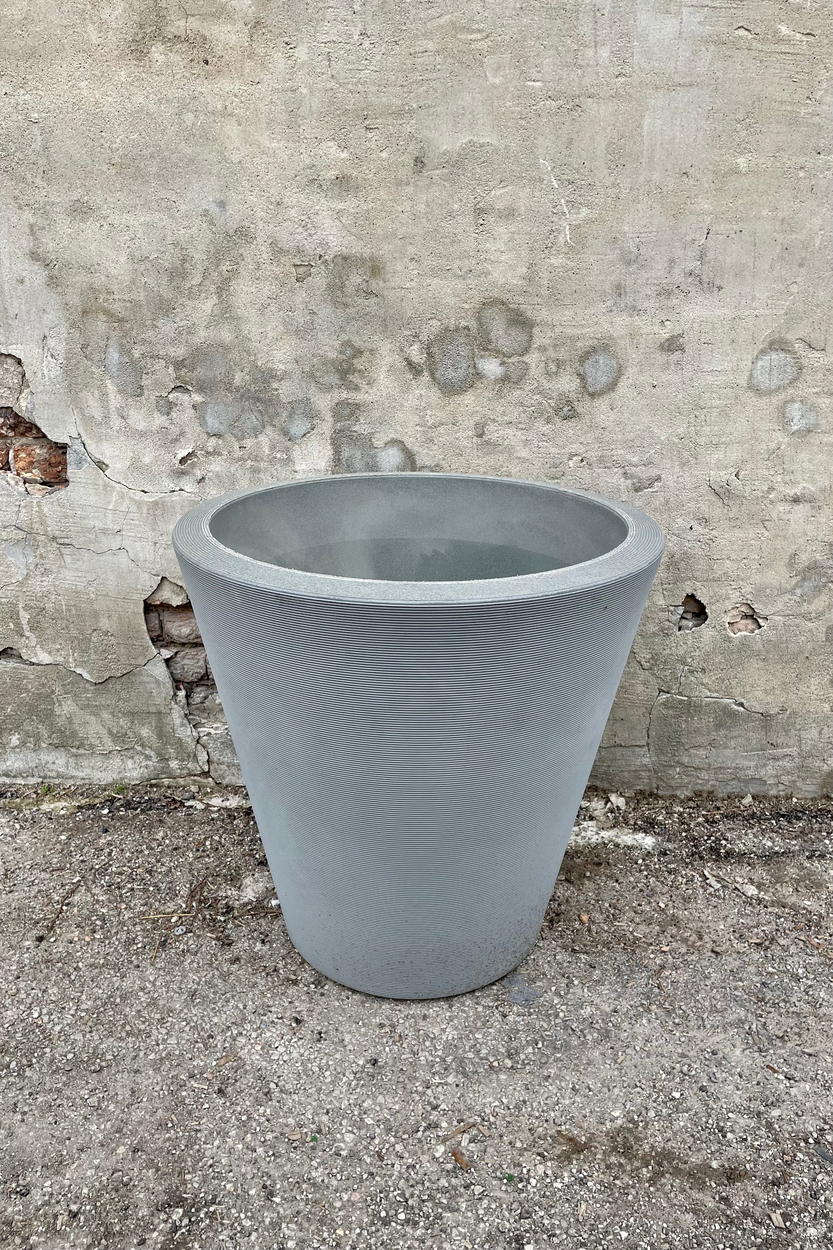 The Weathered grey Madison planter in a 26" diameter against a cement wall.