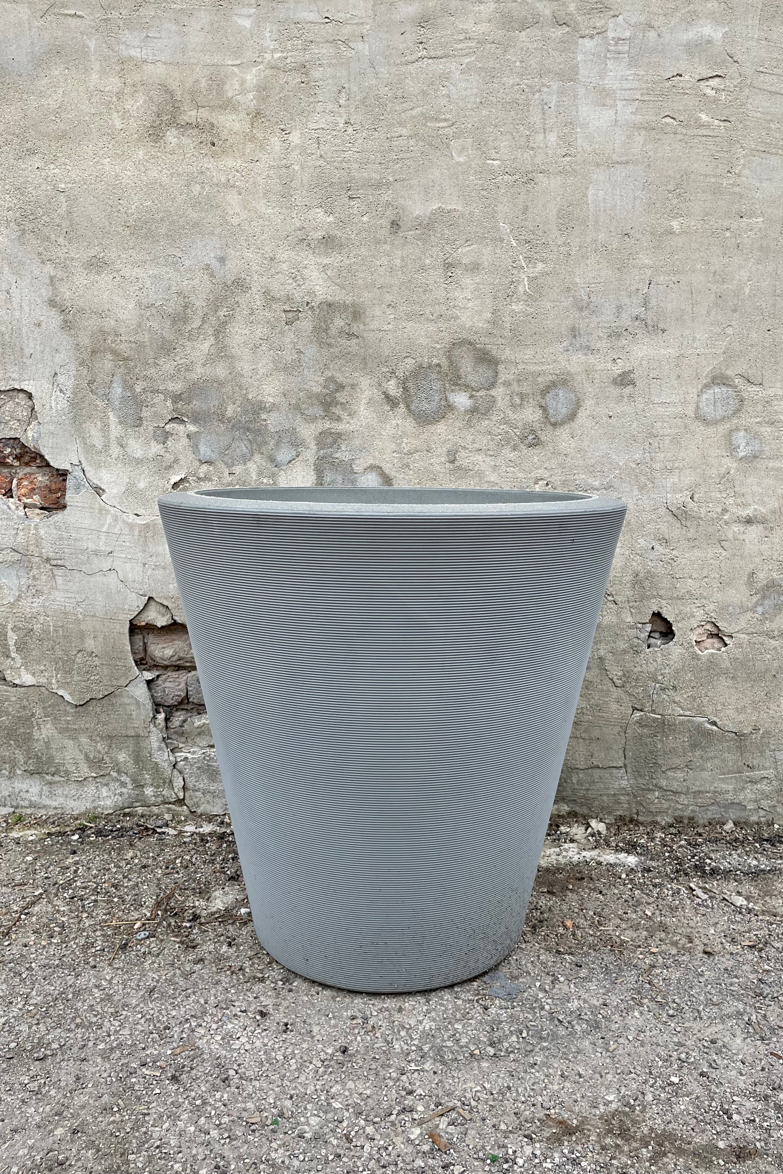 The Weathered grey Madison planter in a 26" diameter against a cement wall.