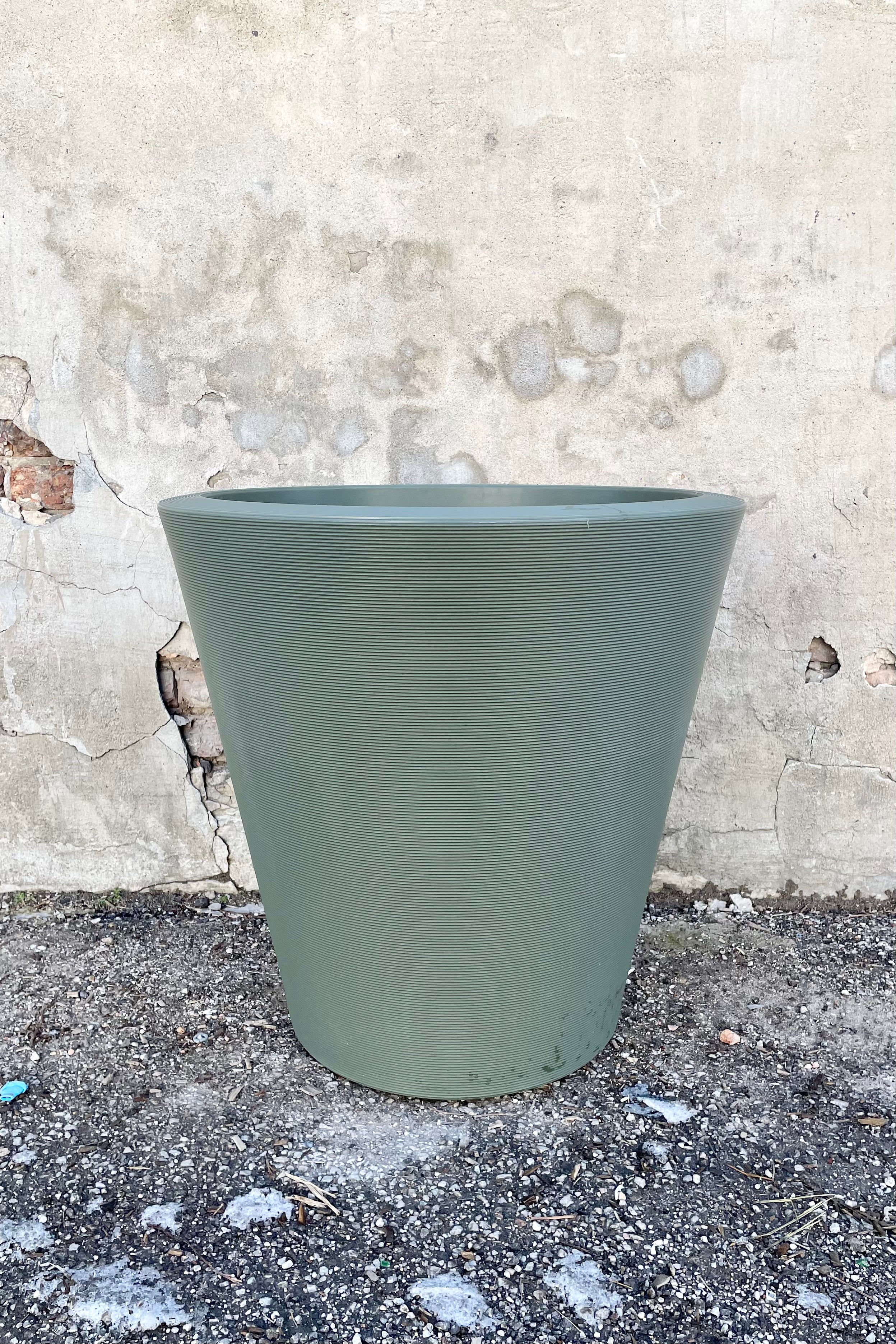 The olive 26" Madison planter against a concrete wall.